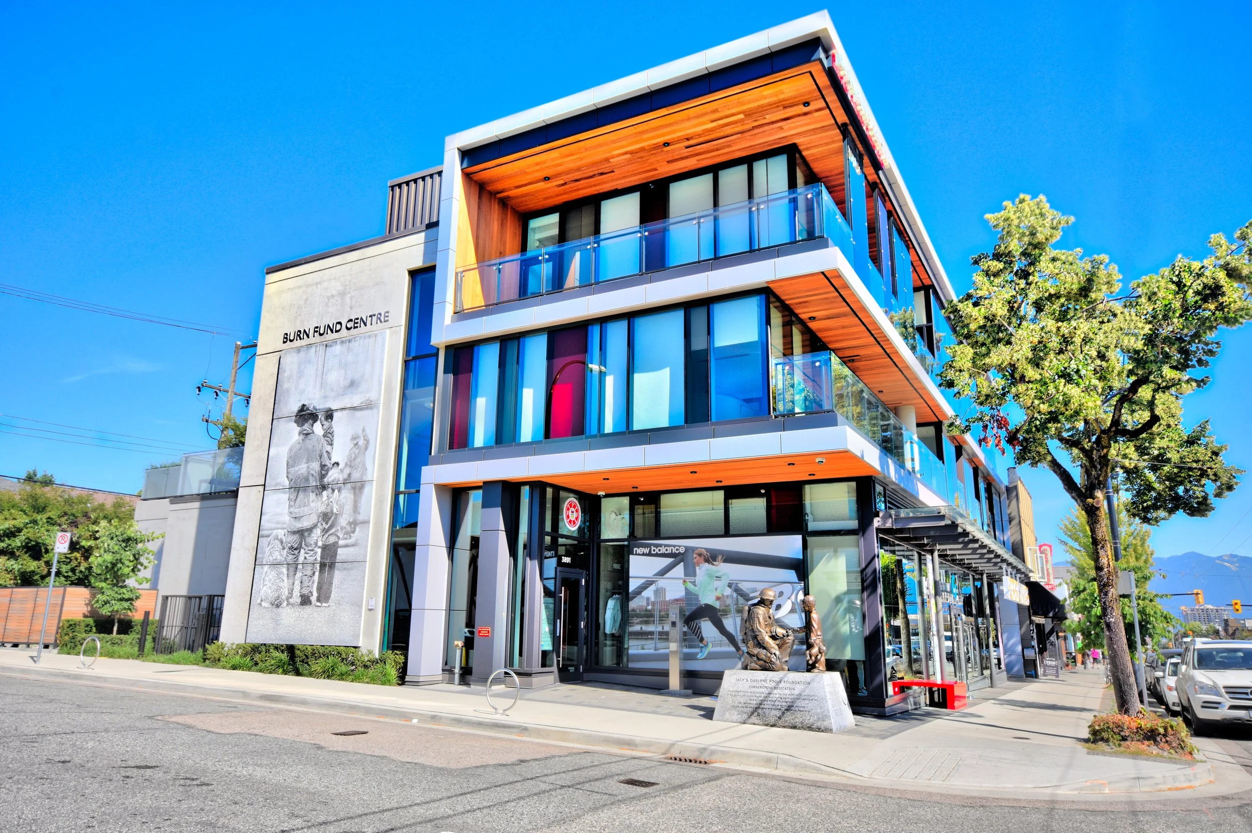 Modern building with glass balconies and a sign that reads "Burn Fund Centre" on the front wall, on a sunny day with clear blue sky and trees nearby.