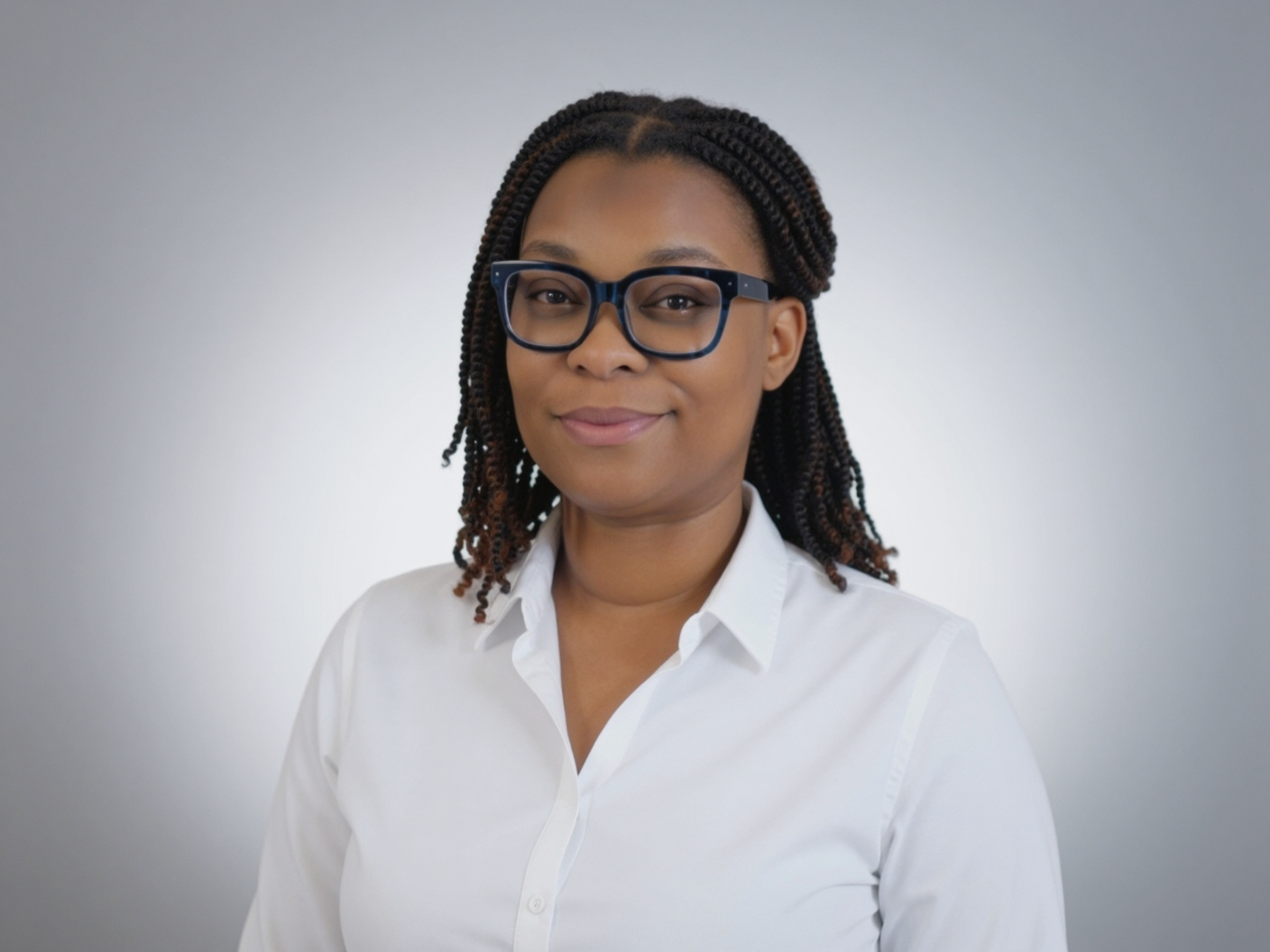 A woman with braided hair wearing glasses and a white shirt, posing against a plain gray background.
