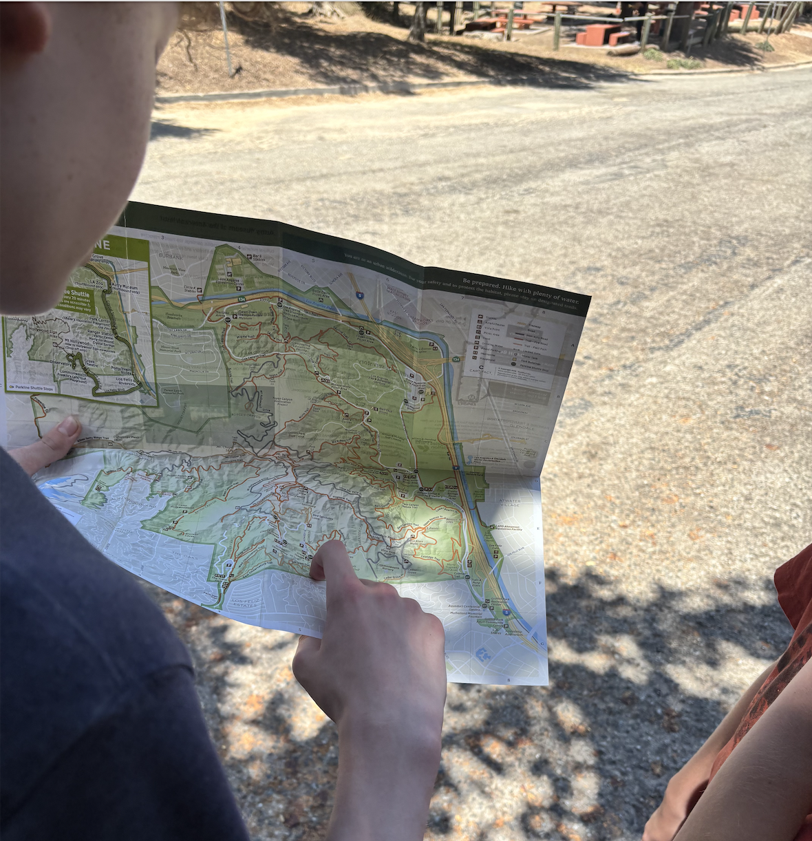 Two people outdoors looking at a detailed trail map of a park or nature reserve.