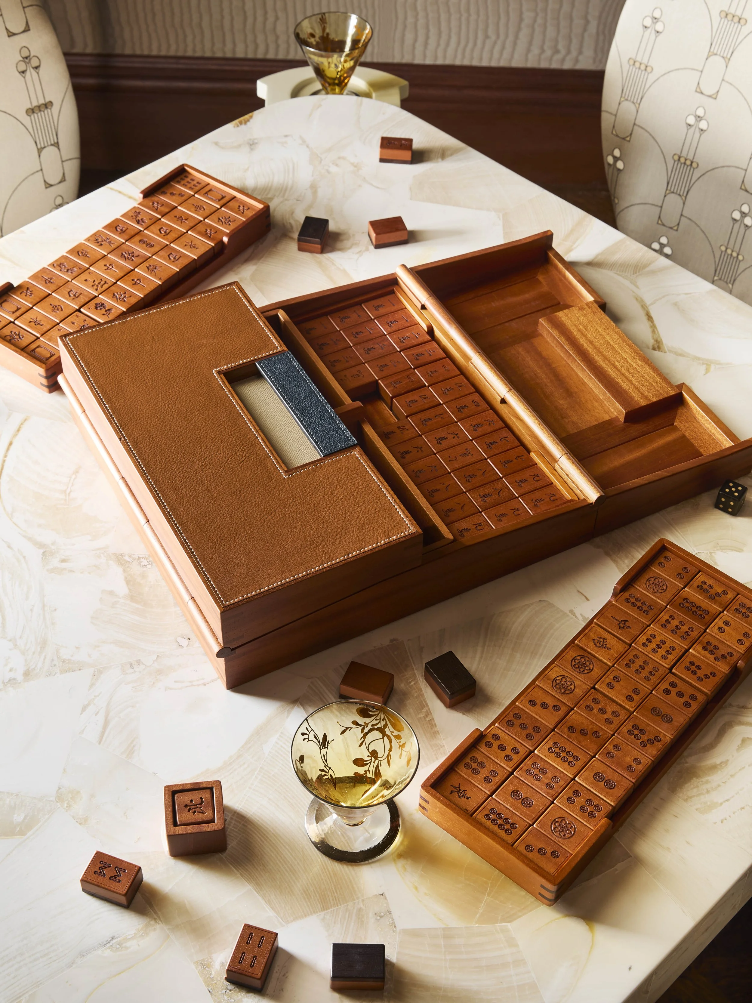 Mahjong game setup on a dining table with wooden tiles, a glass of whiskey, and dice.
