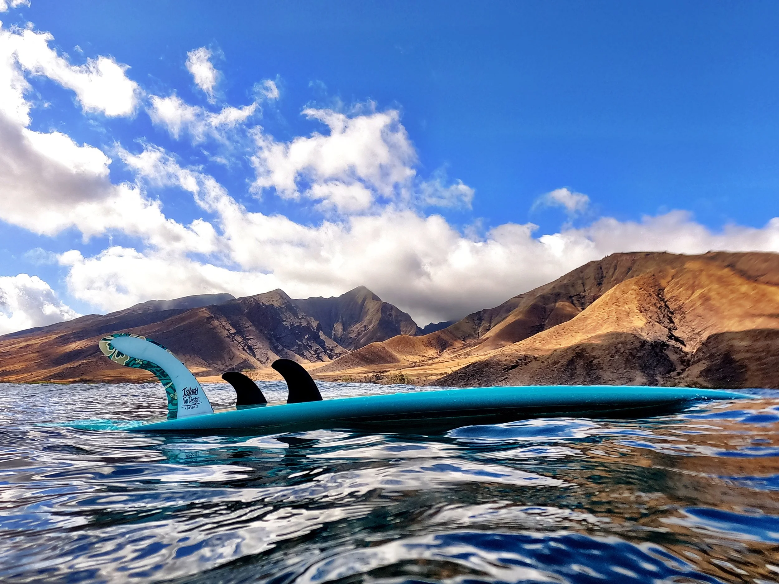 View from water level showing paddleboard with paddle on a lake, mountains and cloudy sky in the background.