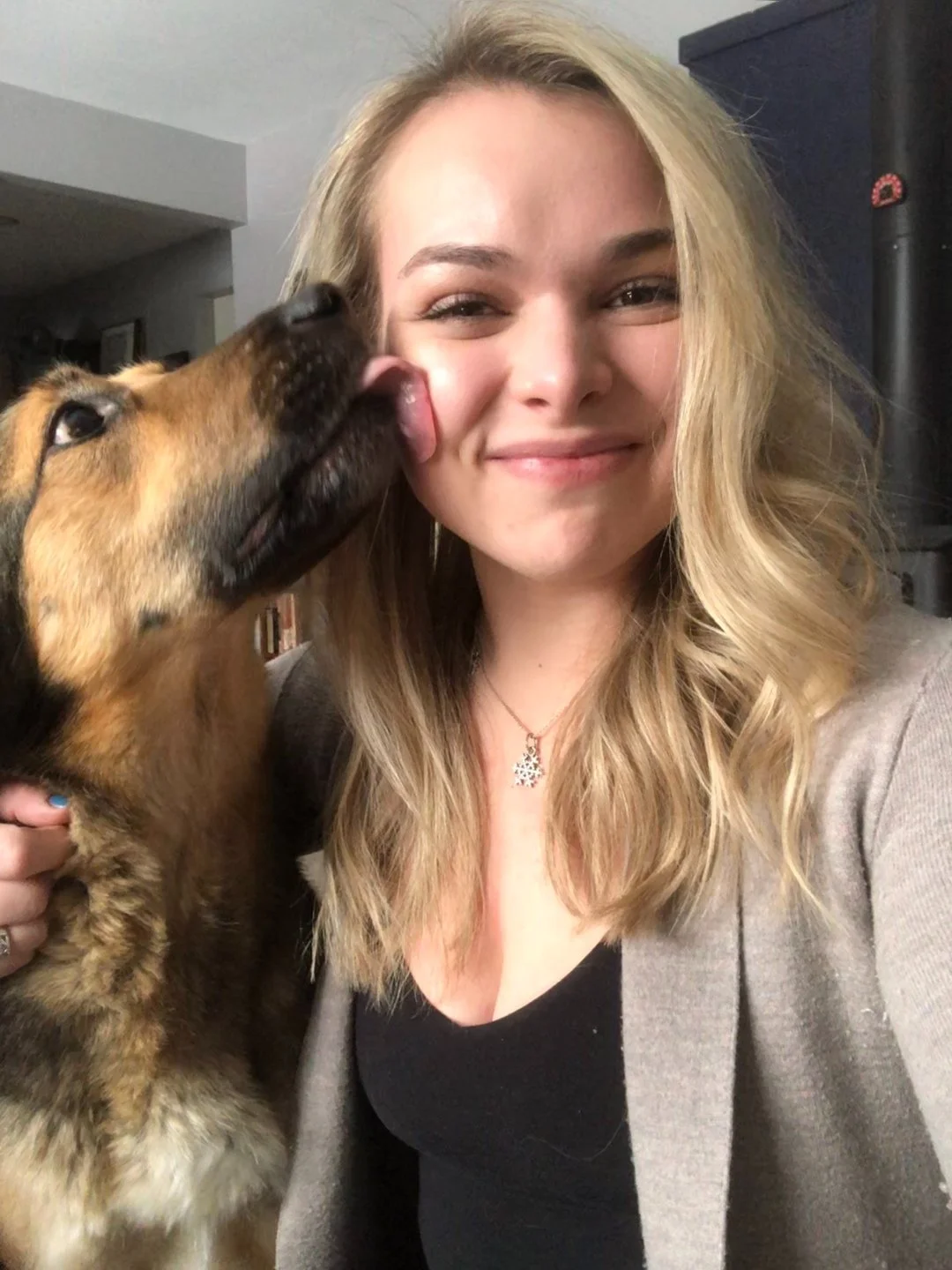 A woman with blonde hair smiling as a dog licks her cheek.