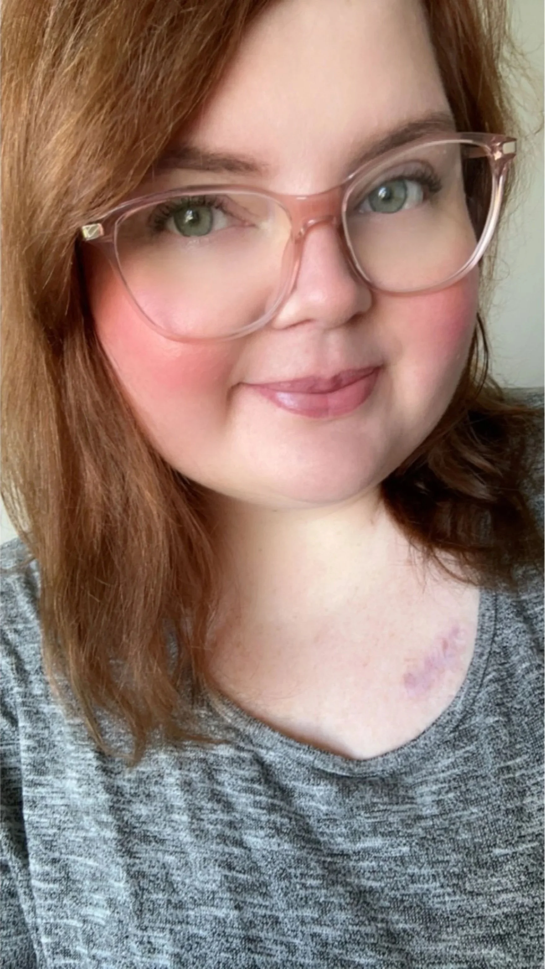 A woman with shoulder-length reddish-brown hair wearing glasses and a gray top, smiling.