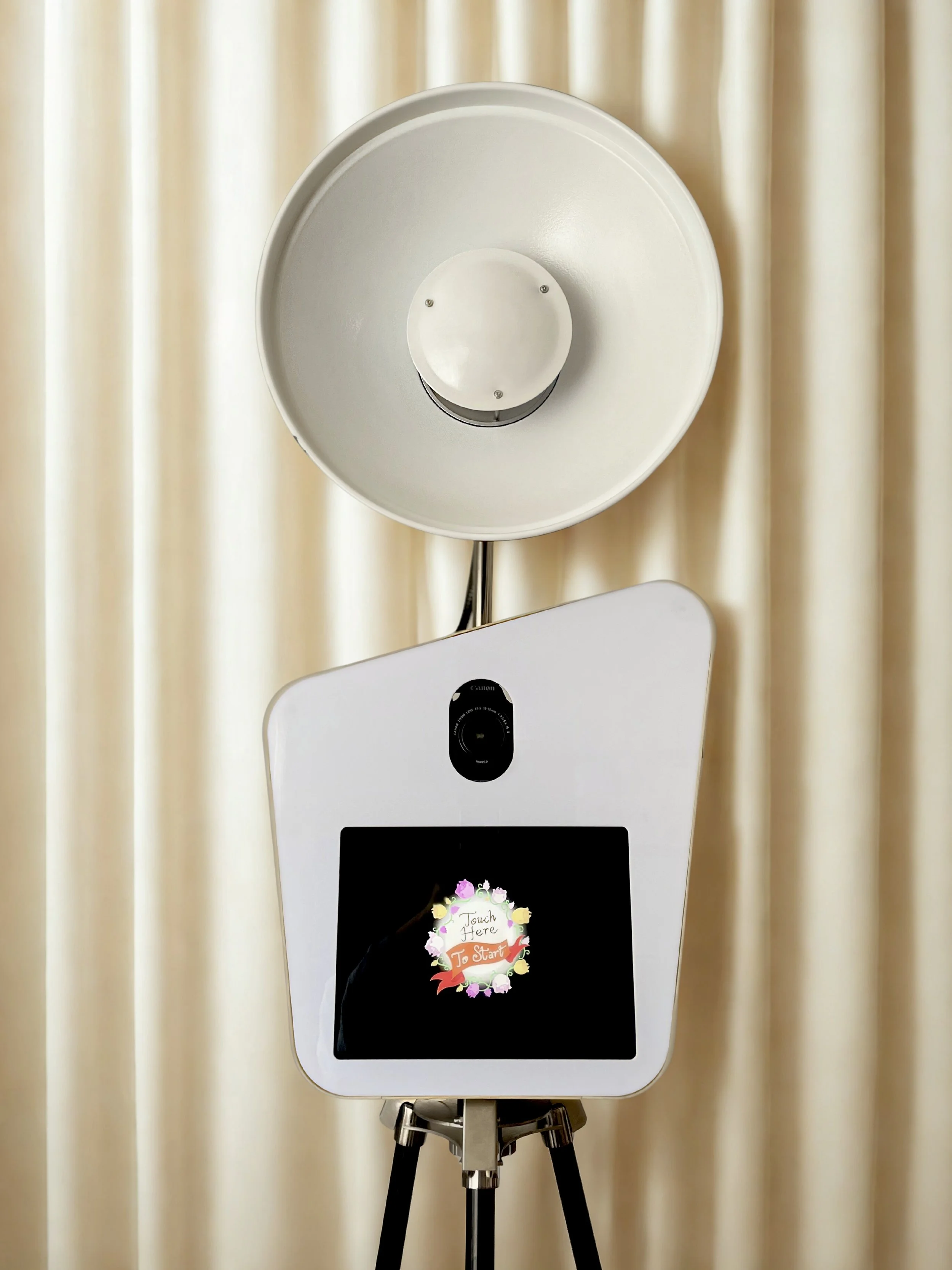 Photo of a photo booth with a large camera lens and a screen displaying an invitation to touch and start.