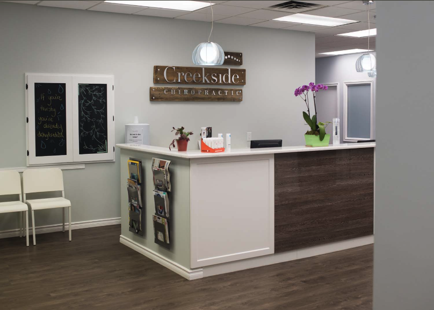 Reception area of Creekside Dynamic Health with a white front desk, purple orchids, chairs, and office decor.
