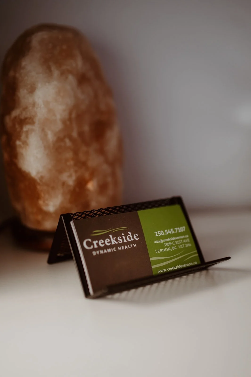 Business card for Creekside Dynamic Health in front of Himalayan salt lamp on a white surface.