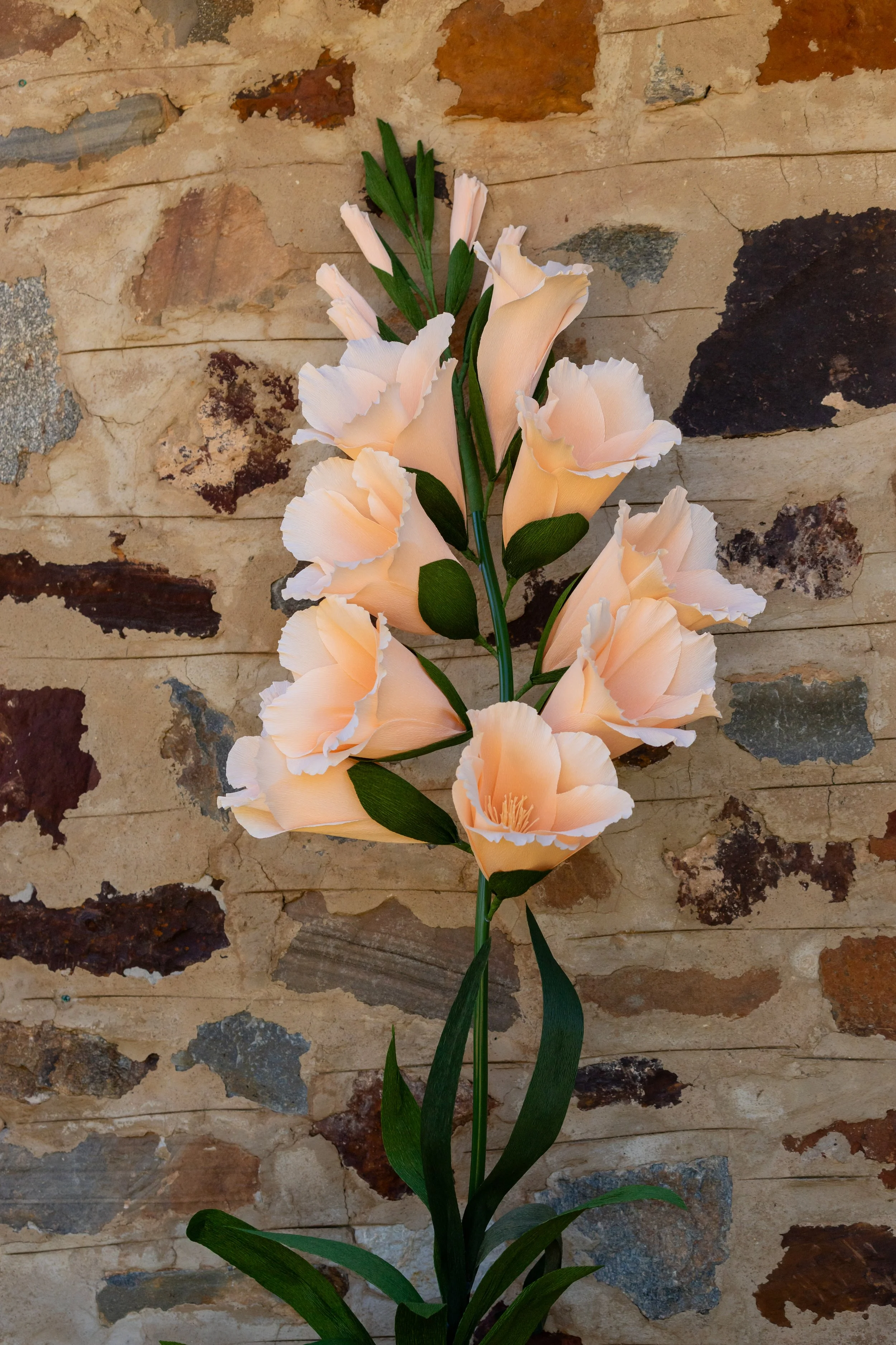 A bunch of pale peach-colored artificial flowers with green leaves against a stone wall background.