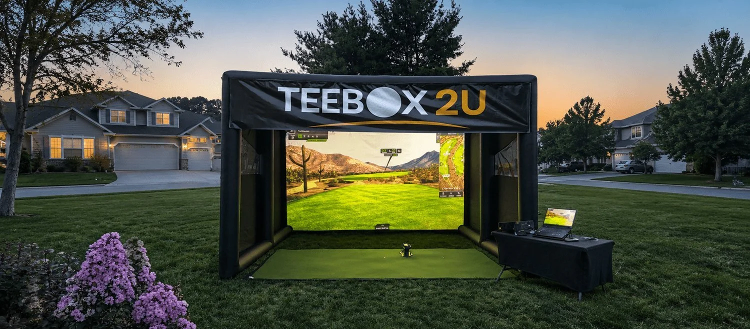 TeeBox2U outdoor mobile golf simulator with a projection screen and equipment table at dusk.