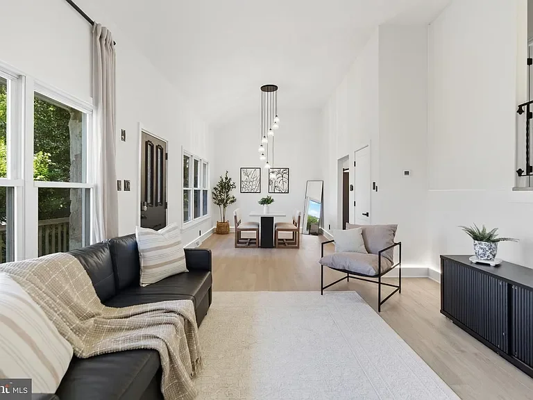 Bright living room with large windows, black and beige sofas, a side table, an armchair, and modern decor including framed artwork and a potted plant.