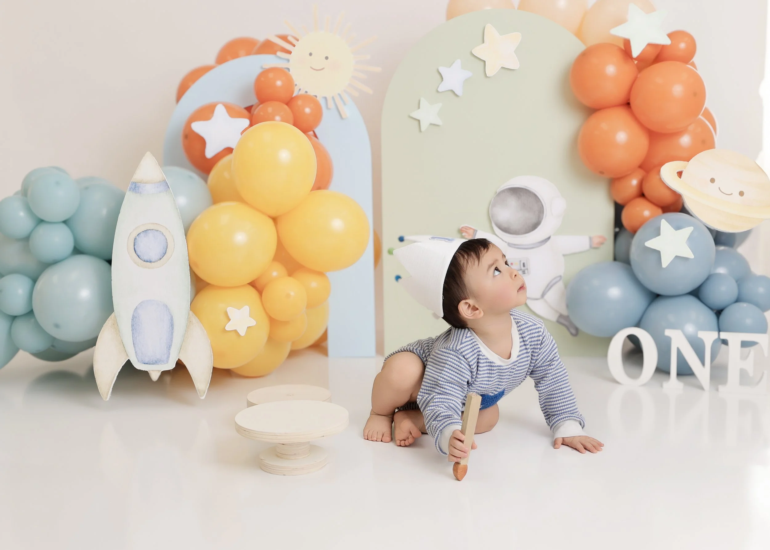 Young child dressed as an astronaut at space-themed birthday party with balloons, planets, stars, and a rocket decoration.