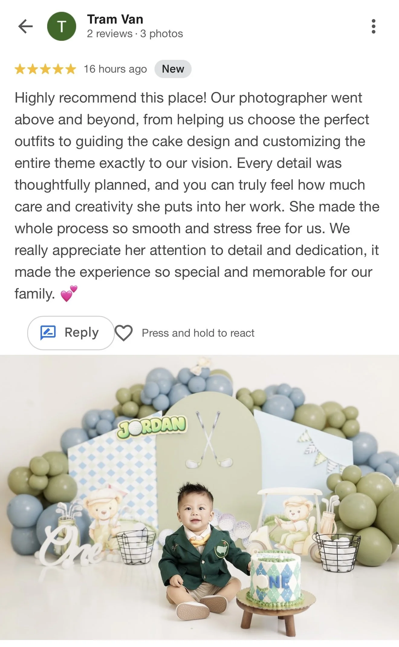 A toddler boy sitting on the floor in front of a birthday cake with a golf theme, surrounded by green and blue balloons, decorations, and toys in a festive setting.