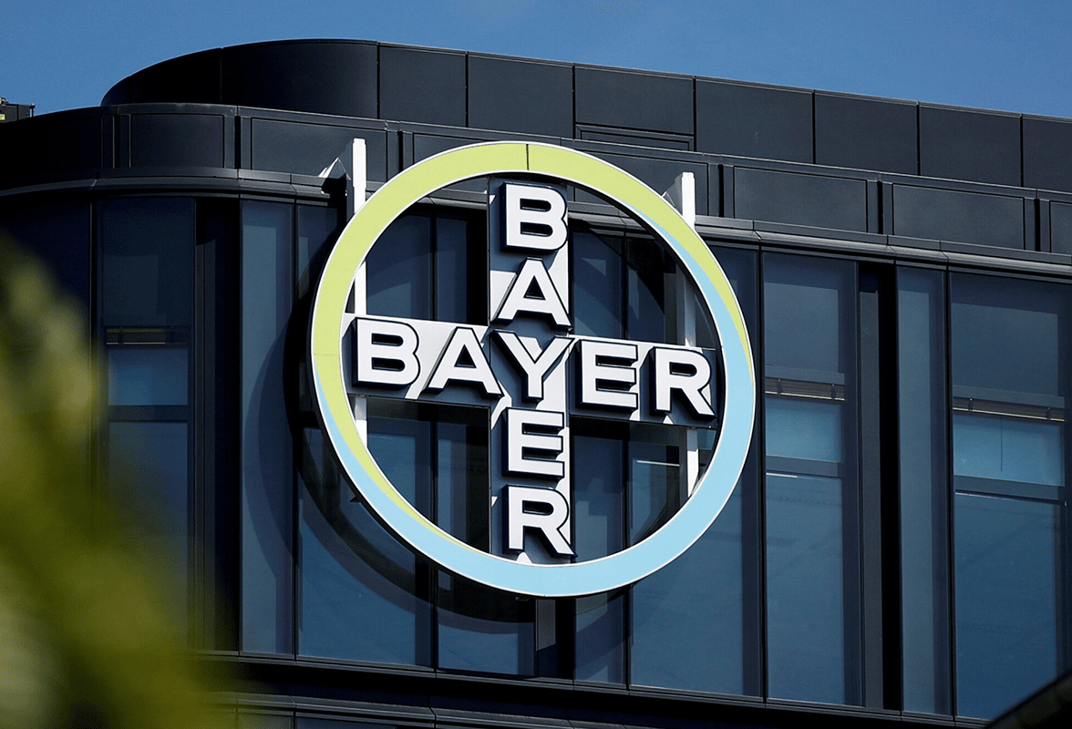 Bayer logo on the side of a modern building with glass windows, circular design with the company name arranged in a plus sign.