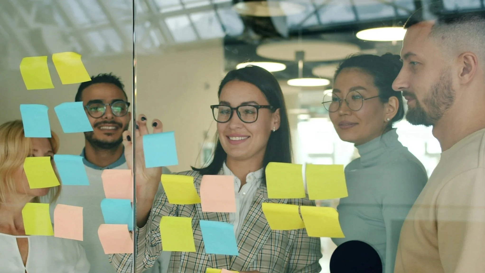 People standing behind glass wall with sticky notes, collaborating in a modern office.