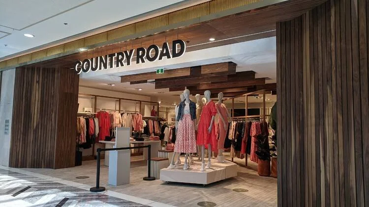 Storefront of Country Road clothing store with mannequins dressed in pink and red dresses, and clothing displays inside.