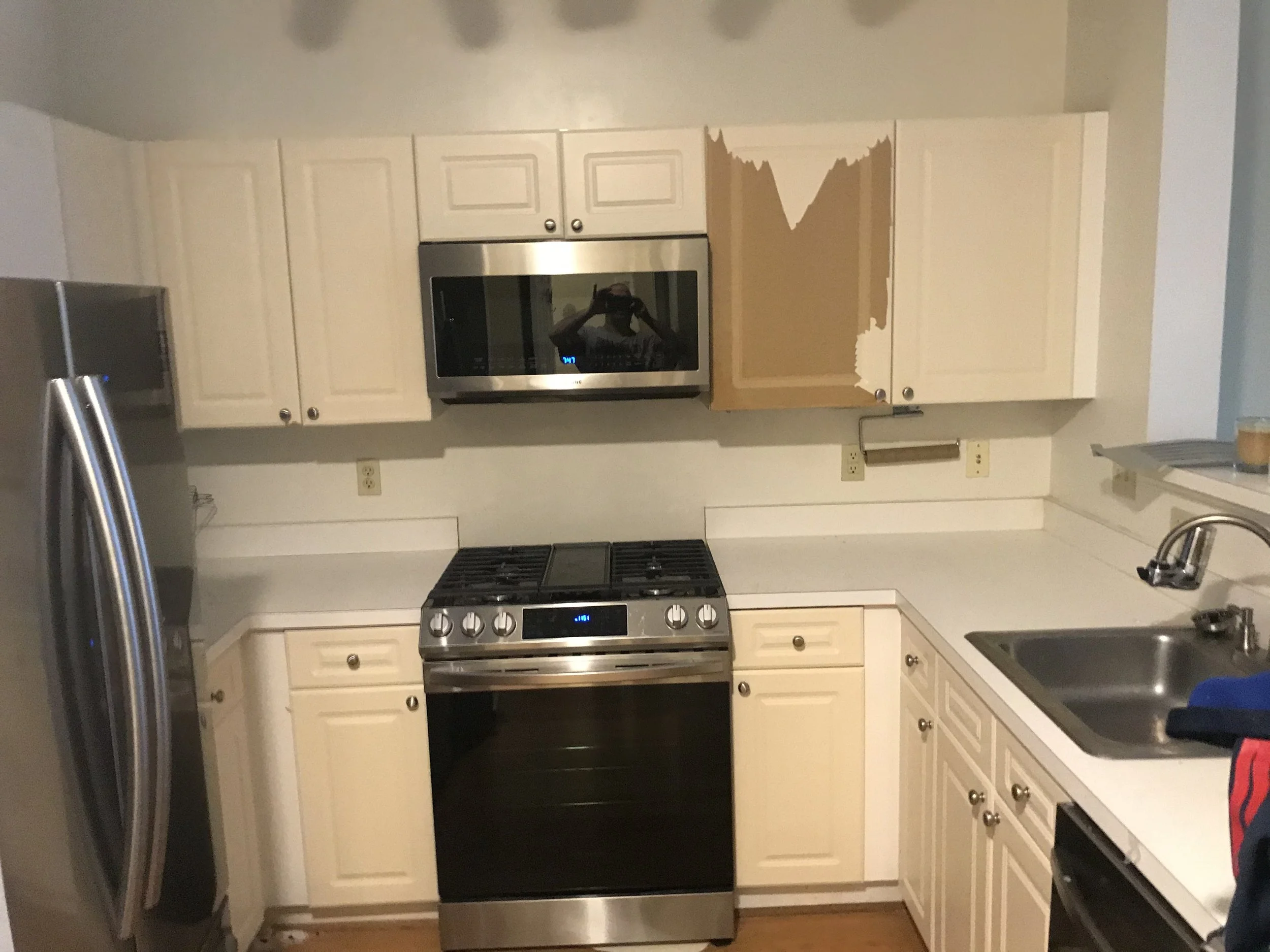 A kitchen with white cabinets, stainless steel appliances including a microwave and oven, and a double sink with a faucet. There are electrical outlets on the wall and a window above the sink.