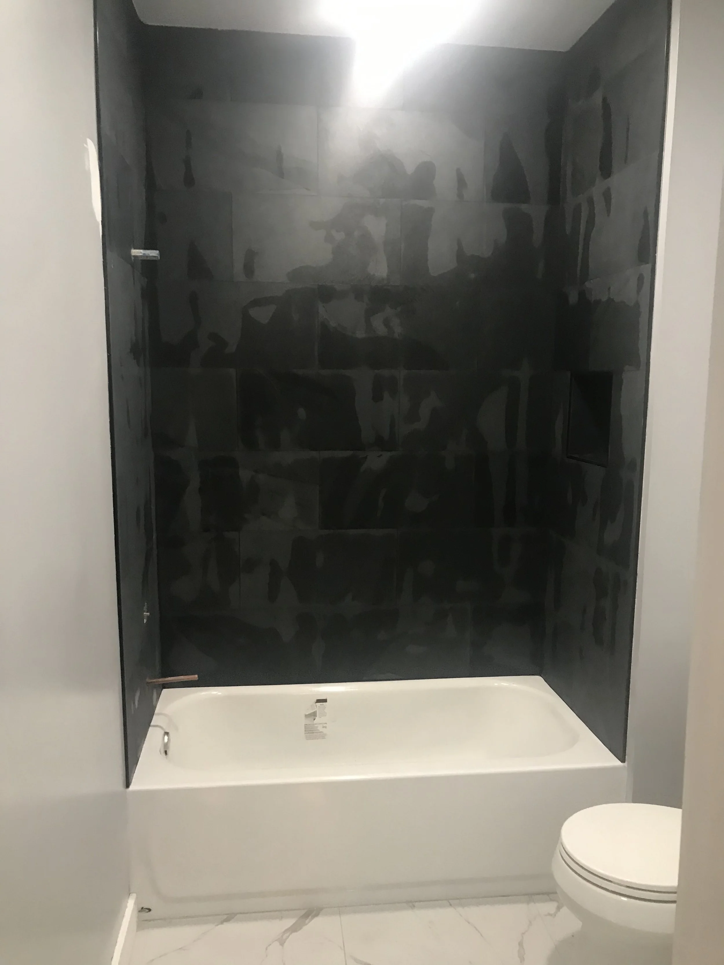 Modern bathroom with a shower enclosure featuring dark tiles, a white bathtub, and a white toilet with a marble floor.