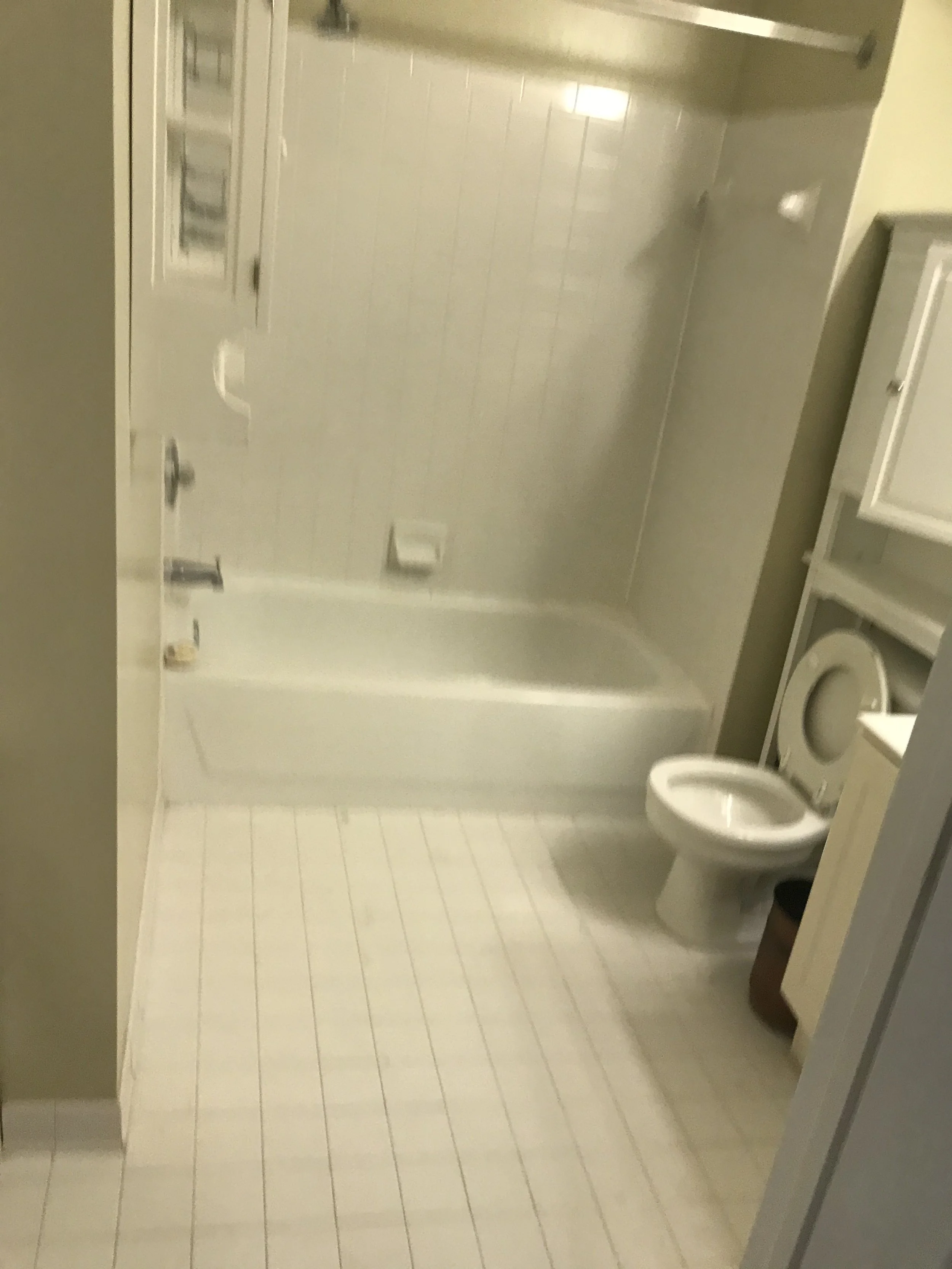 A small bathroom with a toilet and a vanity on the right side. The walls and floor are tiled in light colors. The bathroom appears clean and minimalistic.