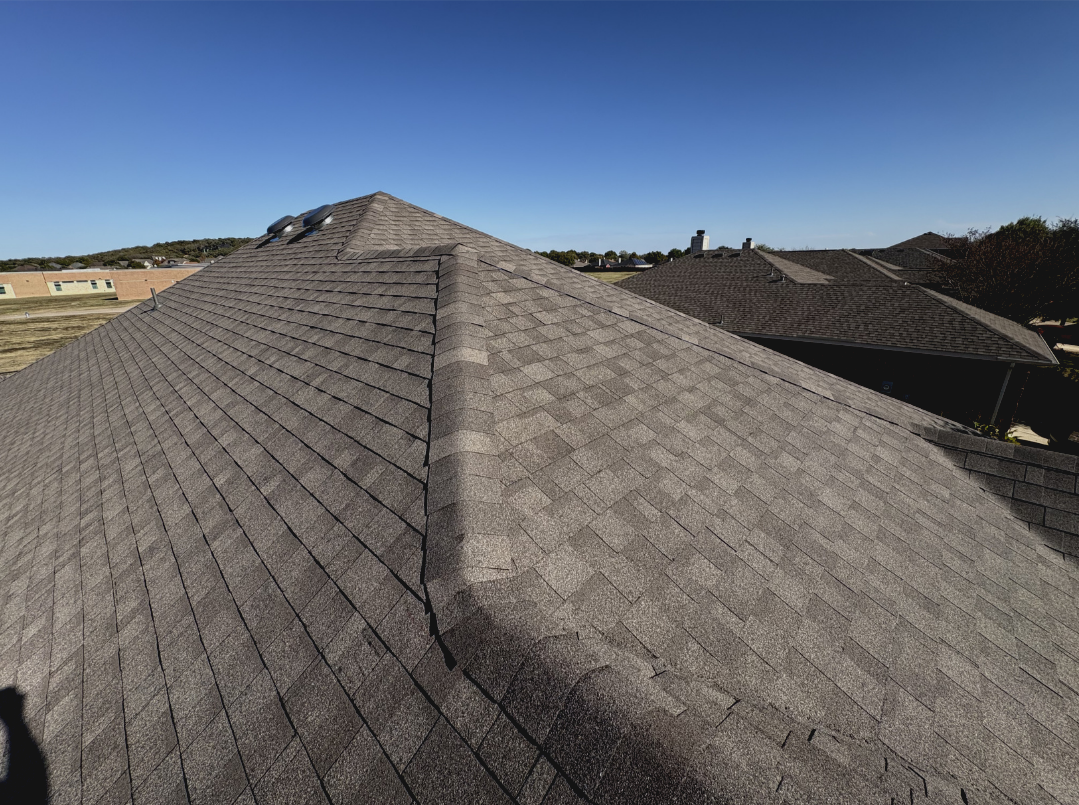 A view of a residential roof with gray shingles under a clear blue sky.