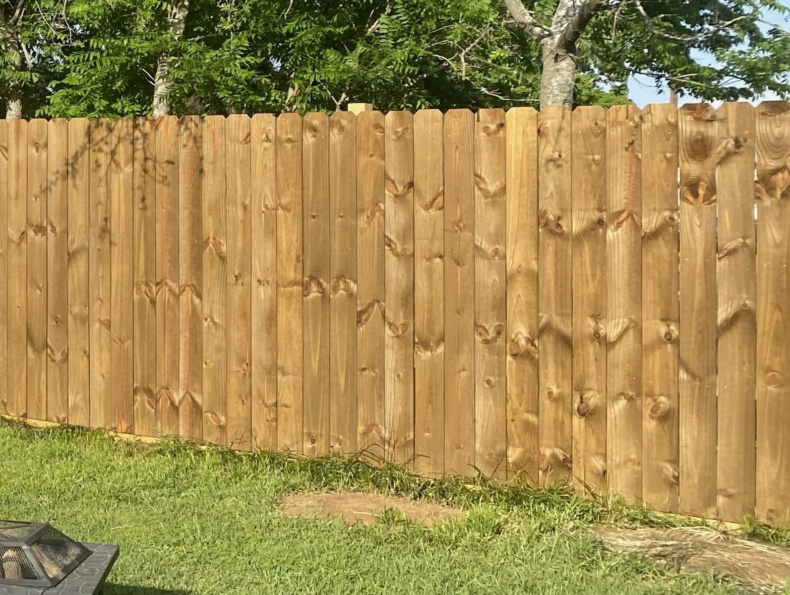 View of a light wooden fence and part of a shed or enclosed structure against a blue sky with scattered white clouds.