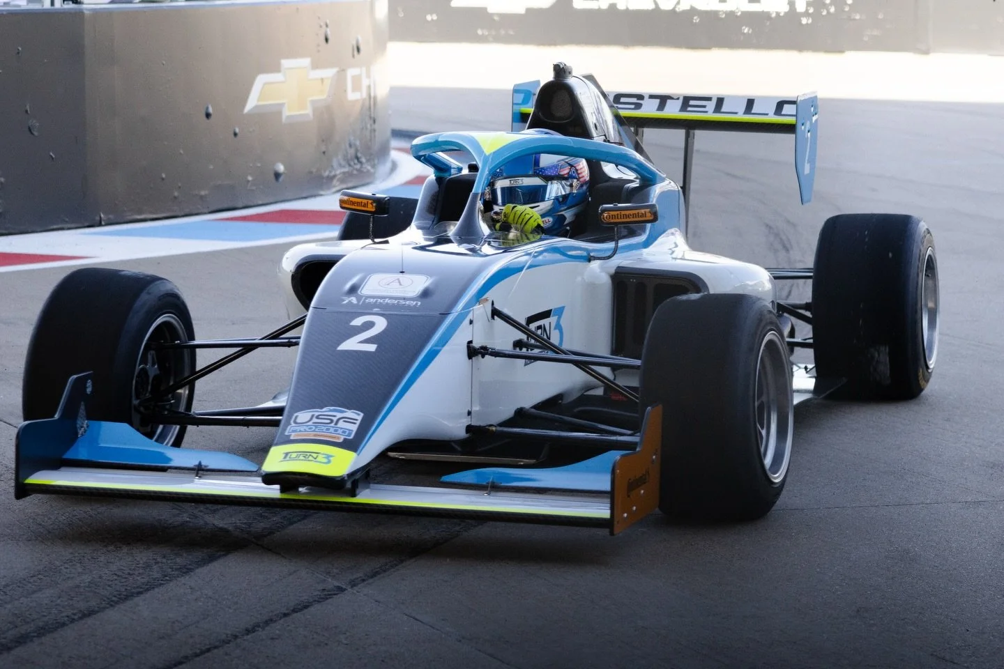 A white and blue open-wheel race car with the number 2, driving on a race track. The car has a prominent rear wing, slick tires, and sponsor logos, including USF Pro 2000.