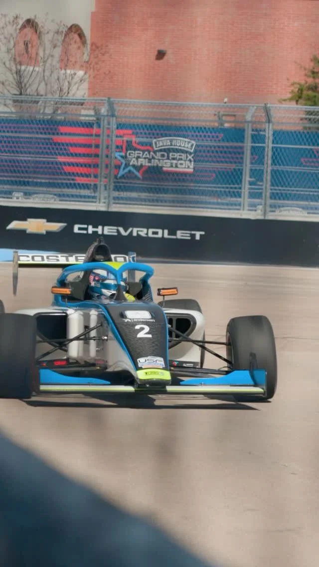 A race car on a track with a banner reading 'Grand Prix Arlington' and 'Chevrolet' in the background.