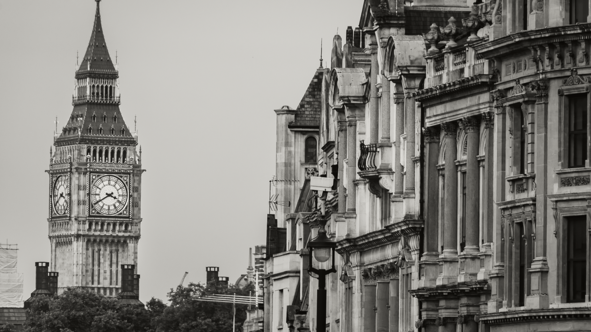Black and white photo of the Big Ben clock tower in London with historic buildings on the right side of the image.