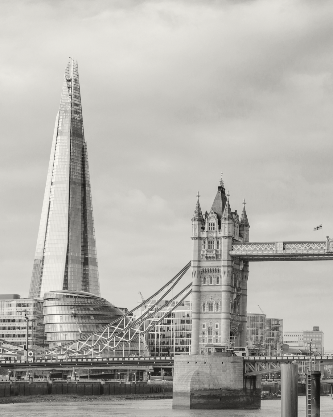Black and white photo of Tower Bridge and The Shard in London, with modern buildings in the background.