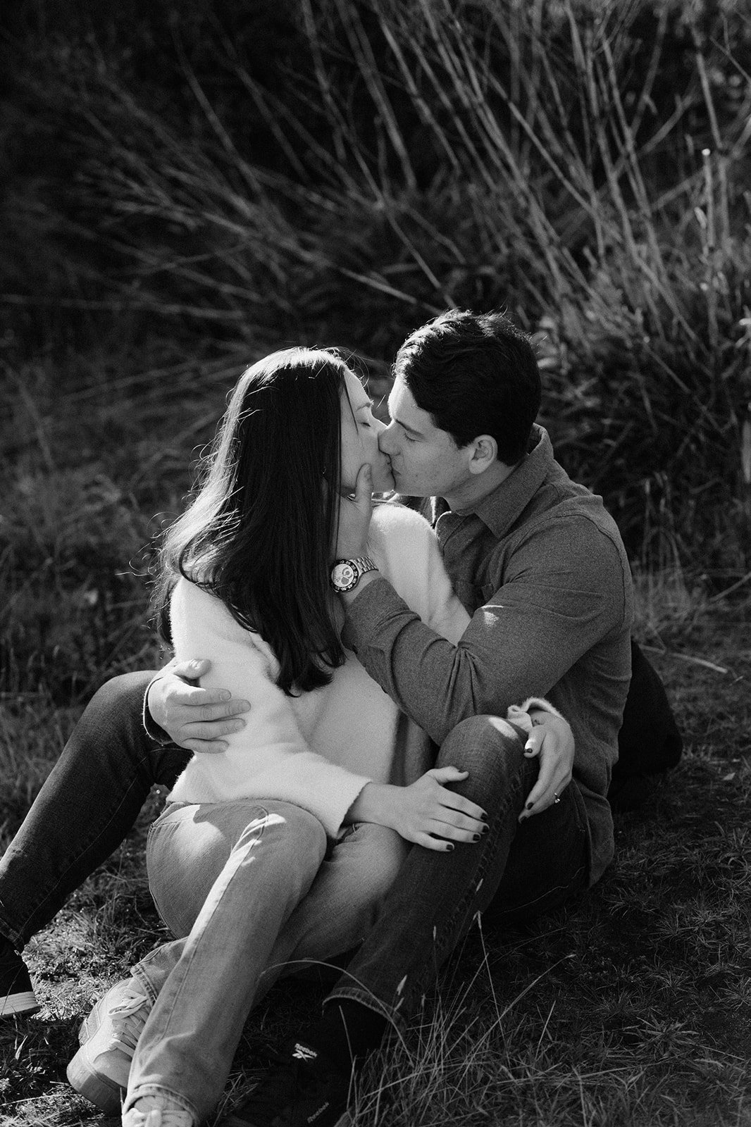 Una pareja se besa y abraza en un entorno natural, en un fondo oscuro con vegetación.
