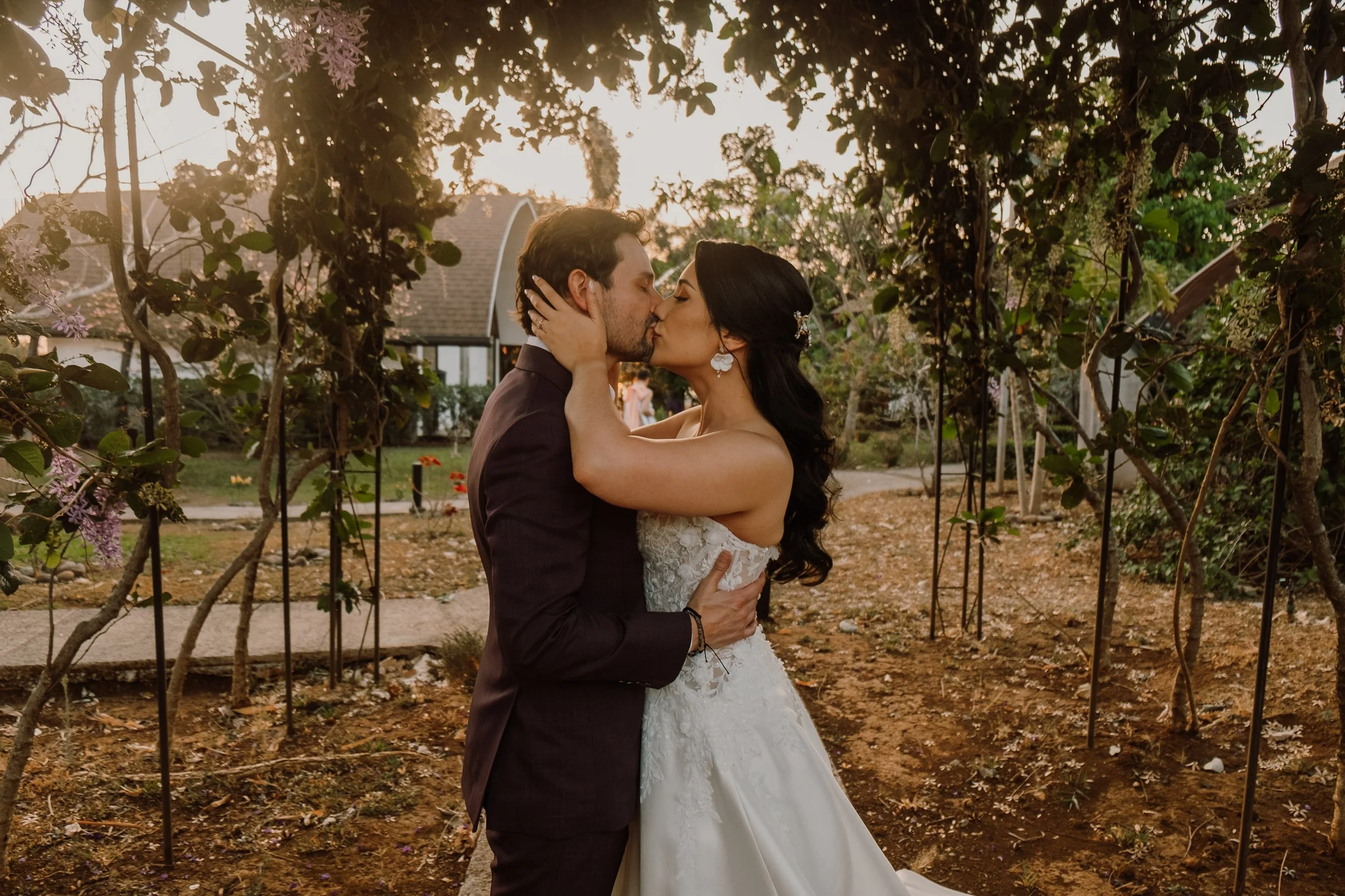 Pareja de novios besándose en jardín al atardecer.