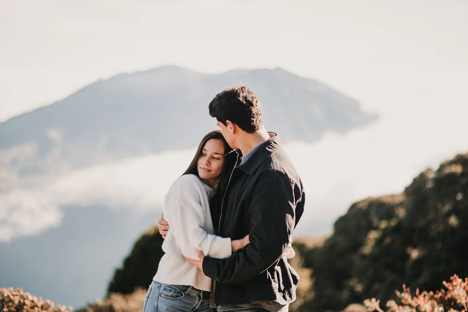 Una pareja abrazándose en un paisaje montañoso y nublado.