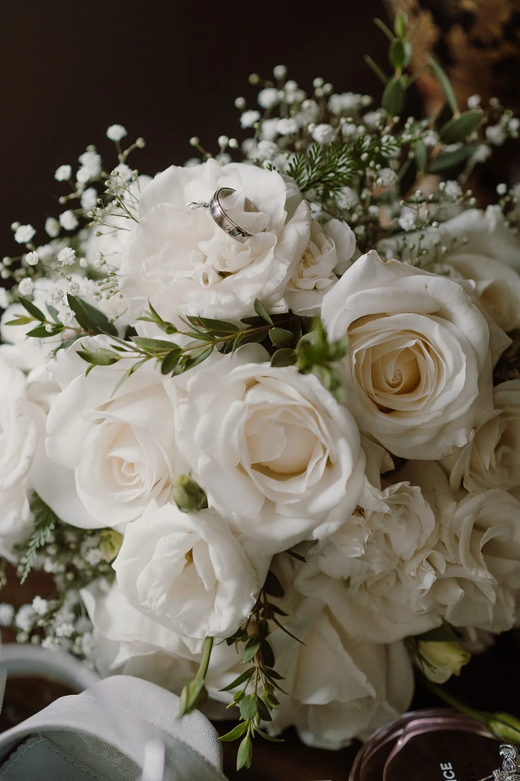 Ramo de flores blancas, incluyendo rosas y otras flores, con anillo de boda en una de las flores.