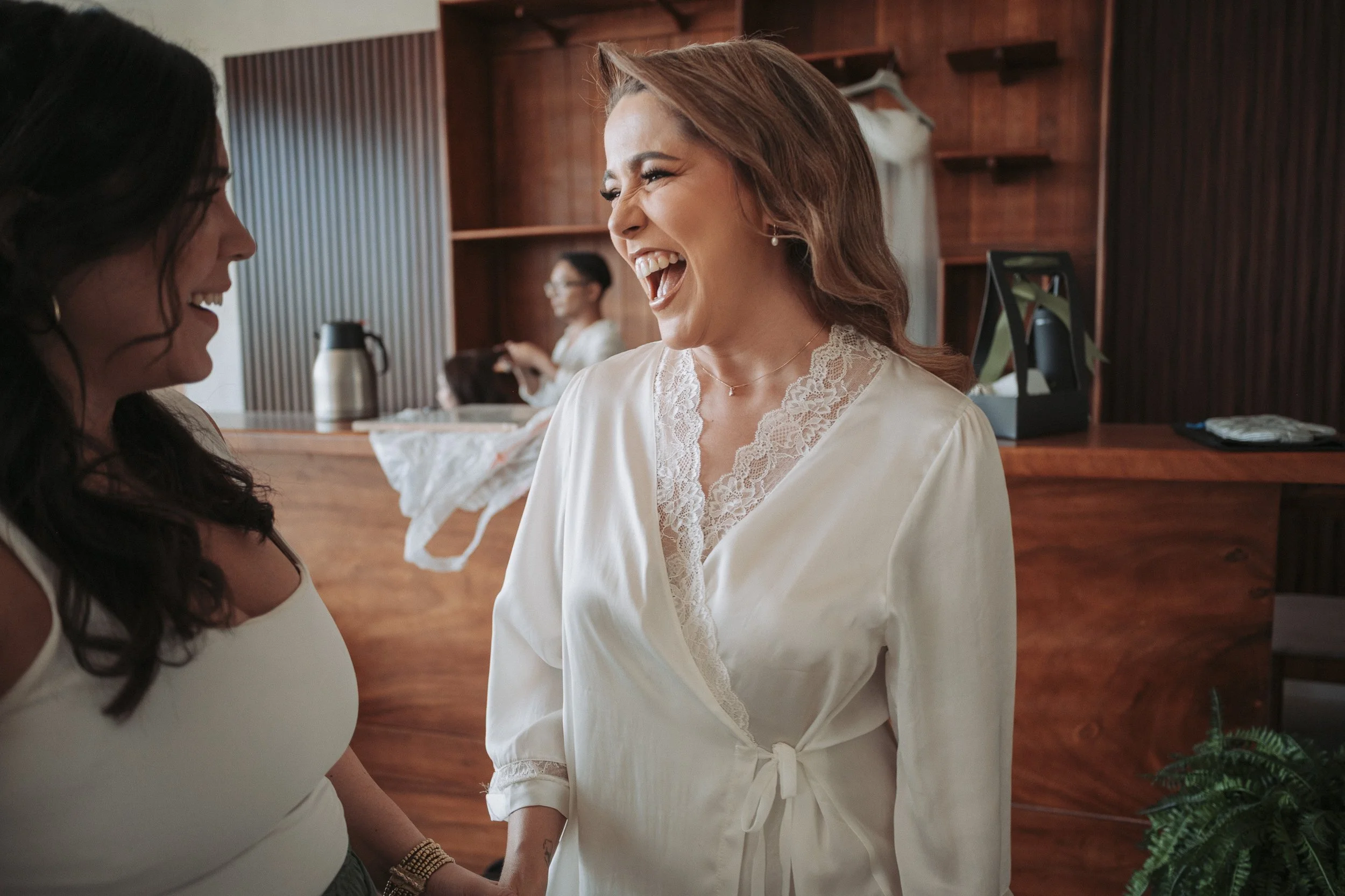 Dos mujeres riendo y hablando en una habitación con madera en el fondo.