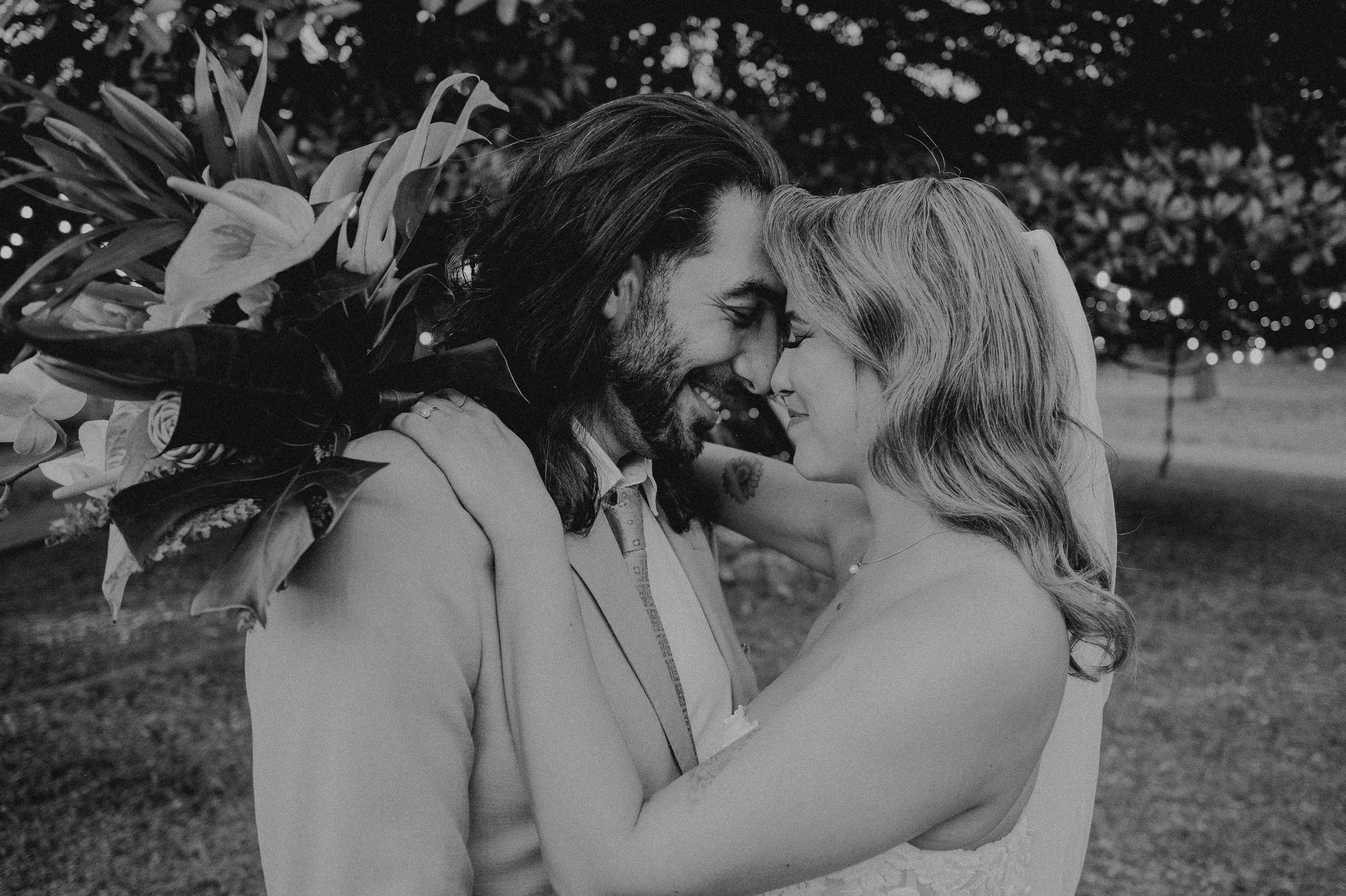Una pareja se abraza y sonríe con las frentes juntas en un entorno al aire libre con luces y árboles