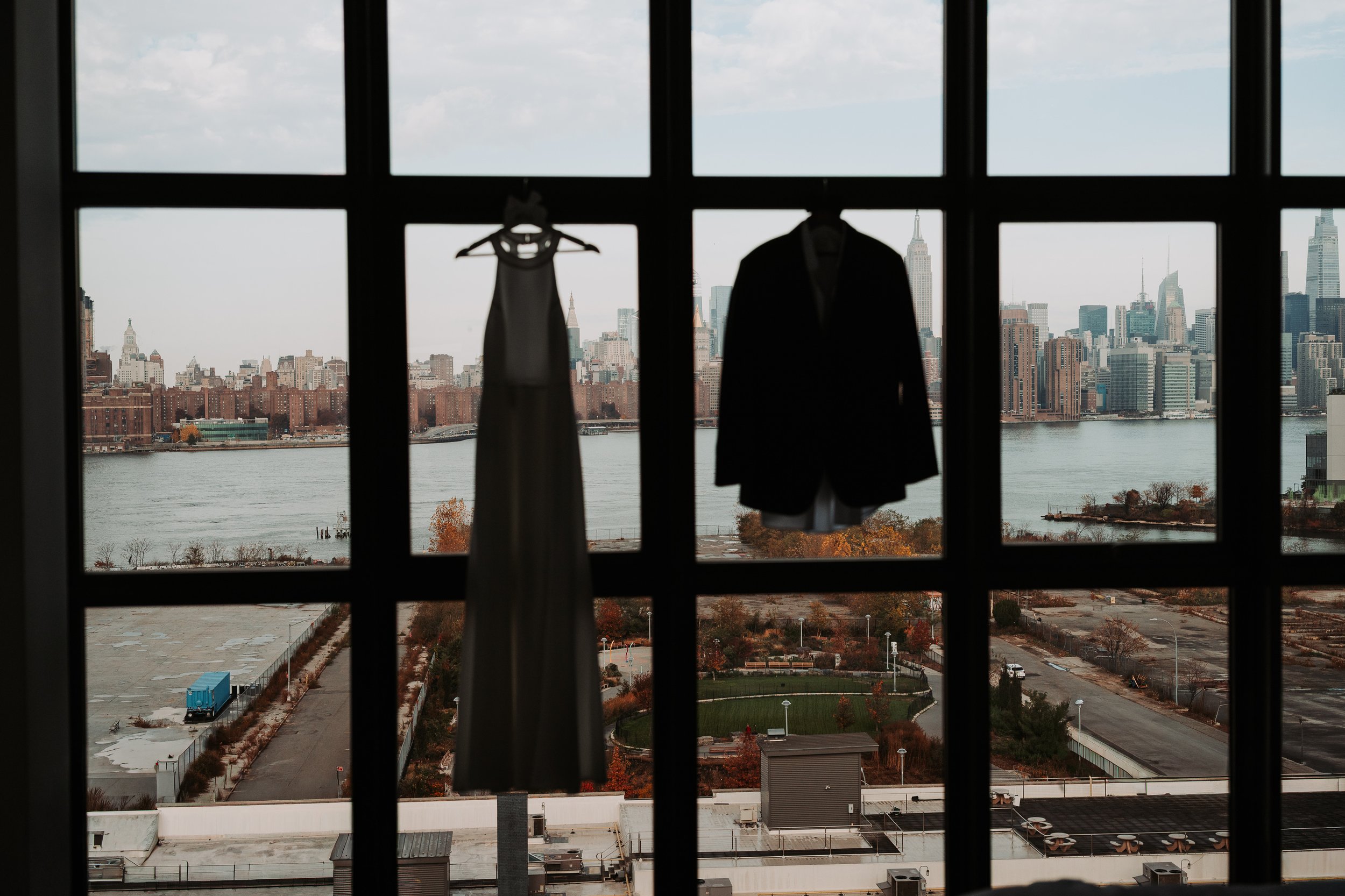 Ropa colgada en una ventana con vista a un río y la ciudad de Nueva York en el fondo, incluyendo el Empire State Building.