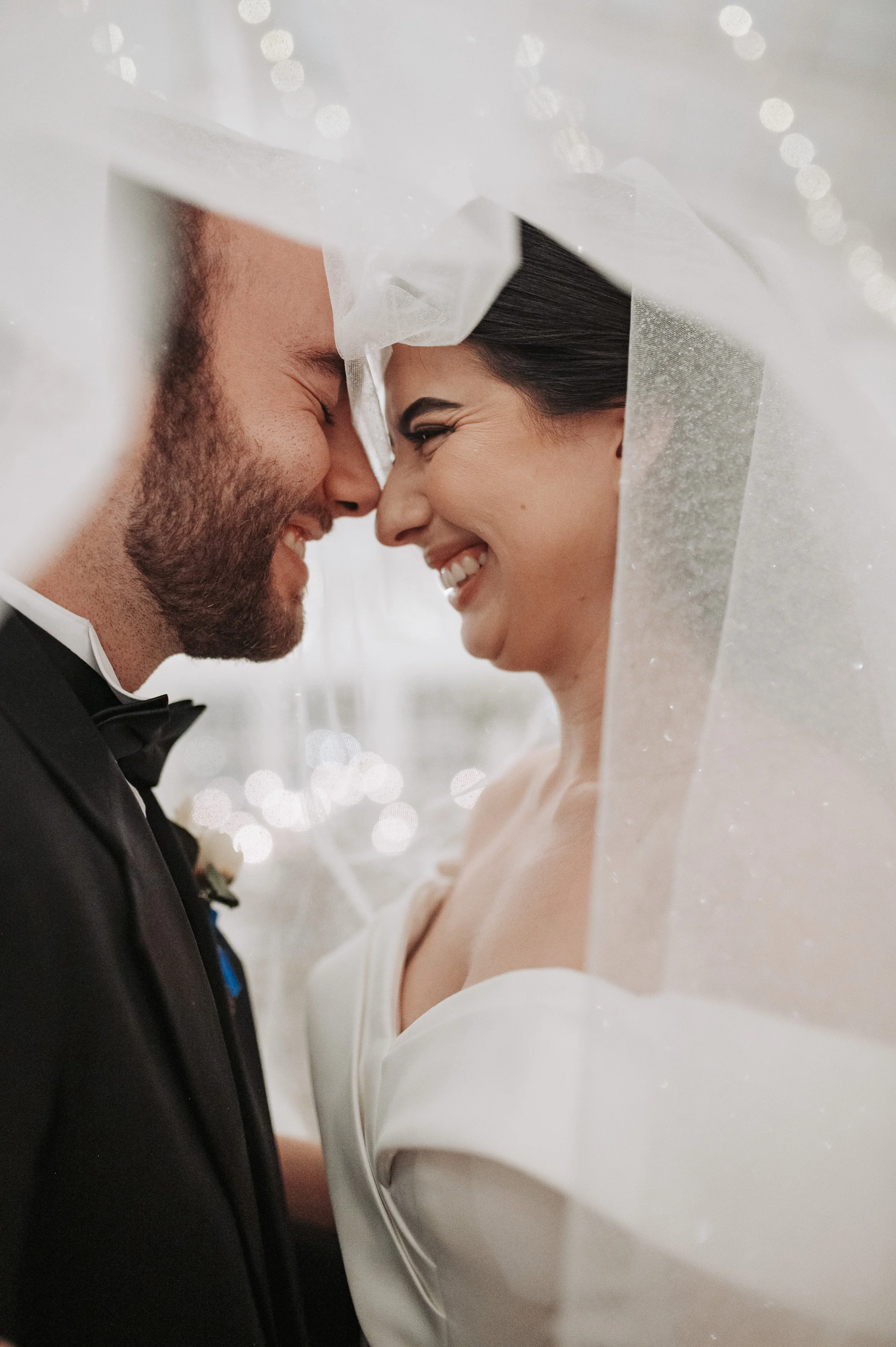Una pareja de novios en su boda, con la frente tocándose y sonriendo, en un momento íntimo y feliz.
