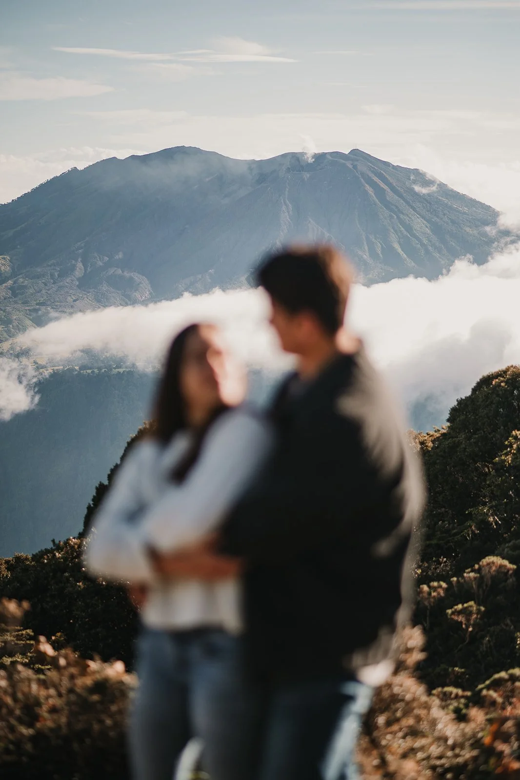 Dos personas abrazadas en primer plano con un volcán y montañas en el fondo.