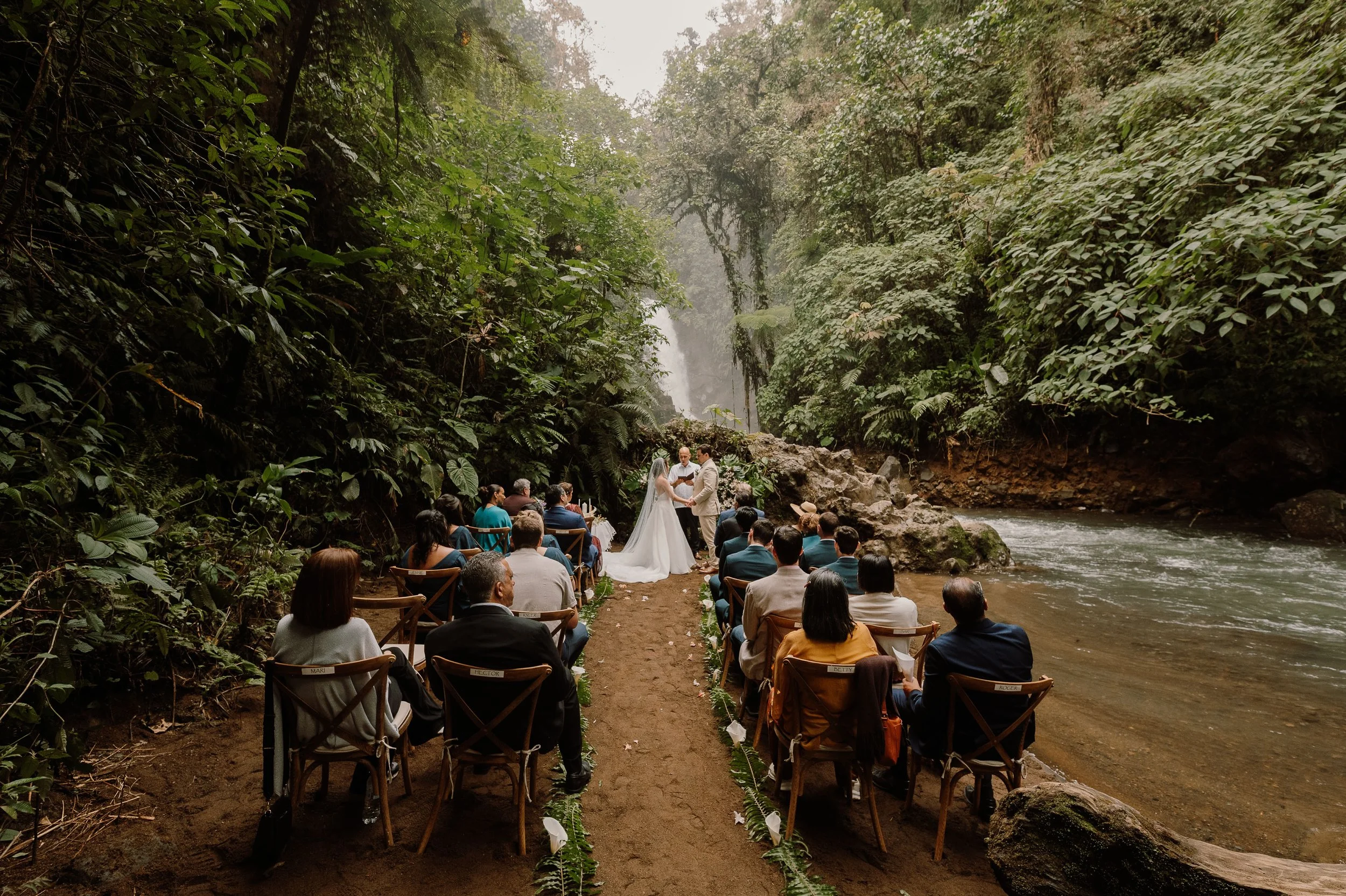 Ceremonia de boda en un bosque junto a un río, con pareja en el altar, rodeada de árboles y vegetación.
