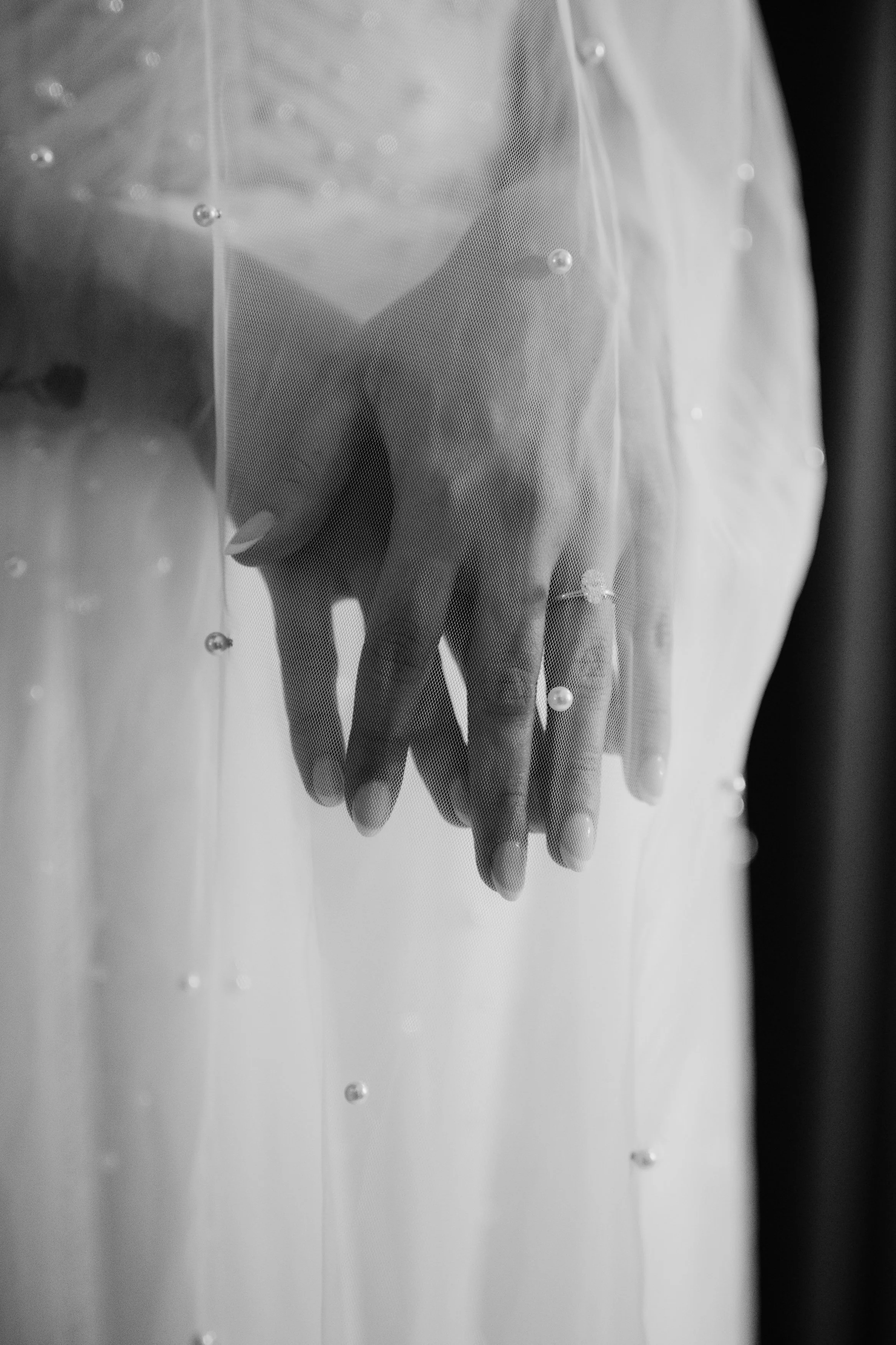 Mano de mujer con anillo, vista a través de una cortina de tul decorada con pequeñas perlas, en color negro y blanco.