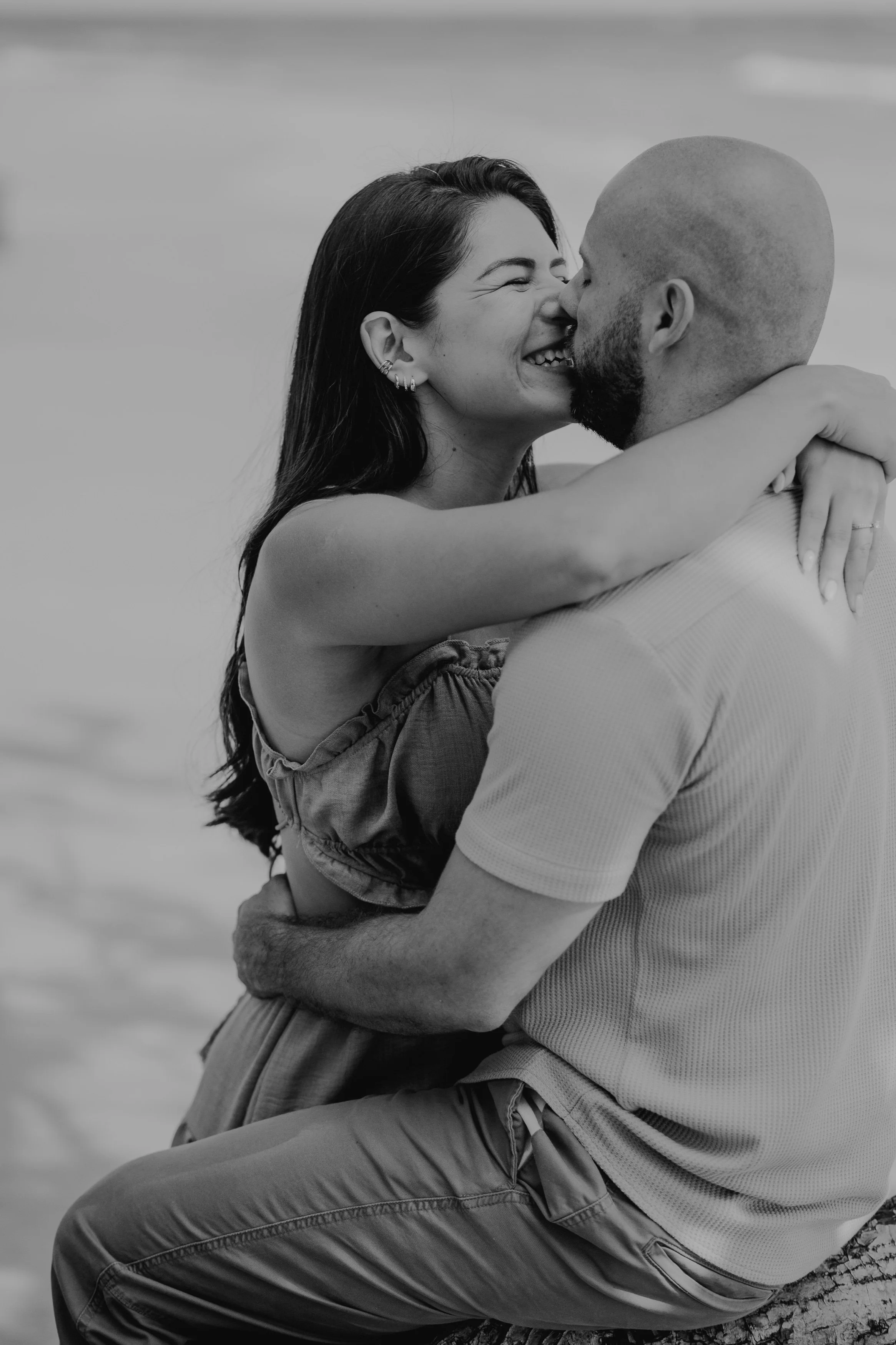 Una pareja abrazada en la playa sonriendo y a punto de besarse, en blanco y negro.