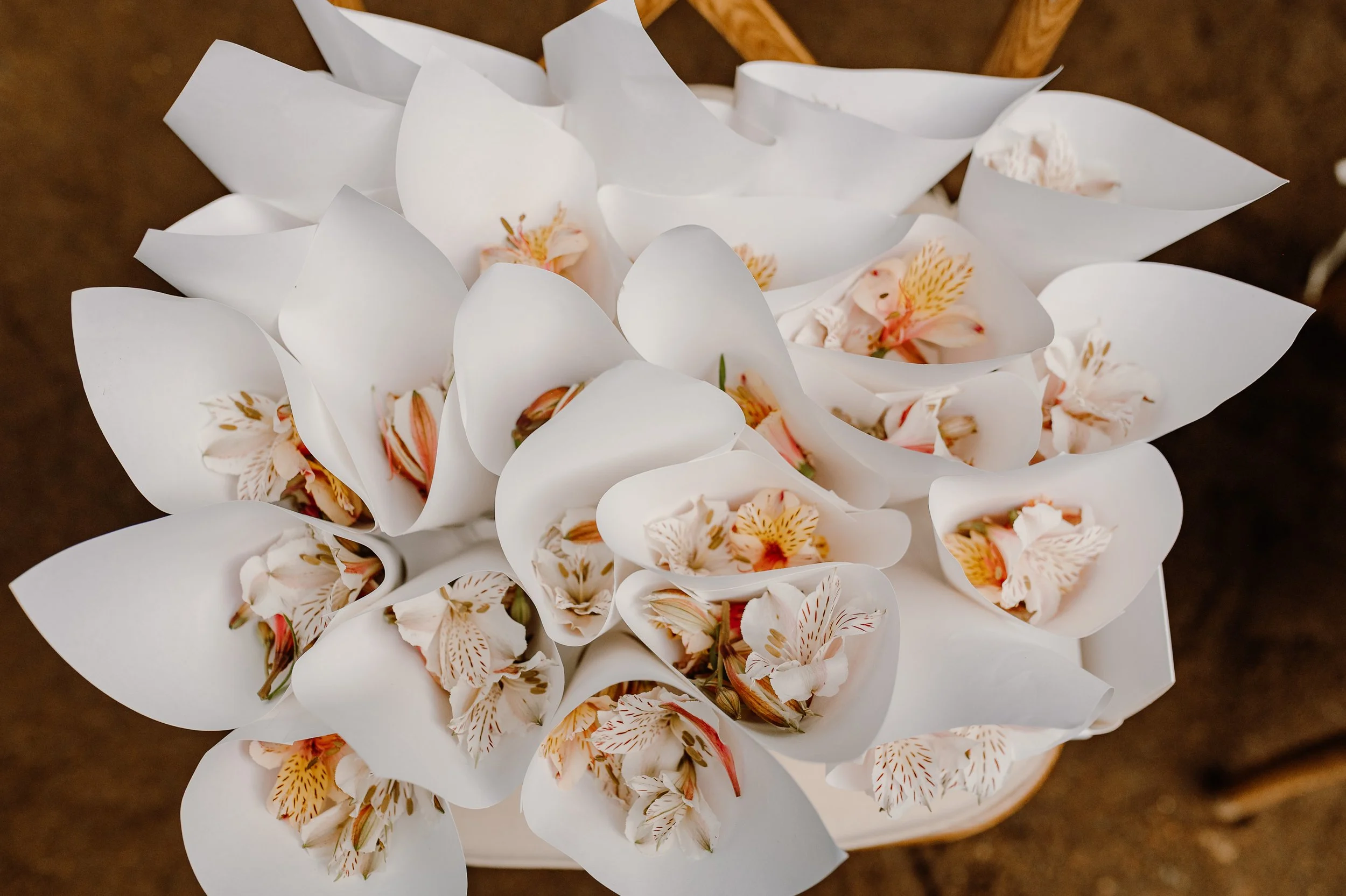 Ramo de flores blancas envueltas en papel blanco, con flores de color rosado y detalles amarillos, en un cesto o caja