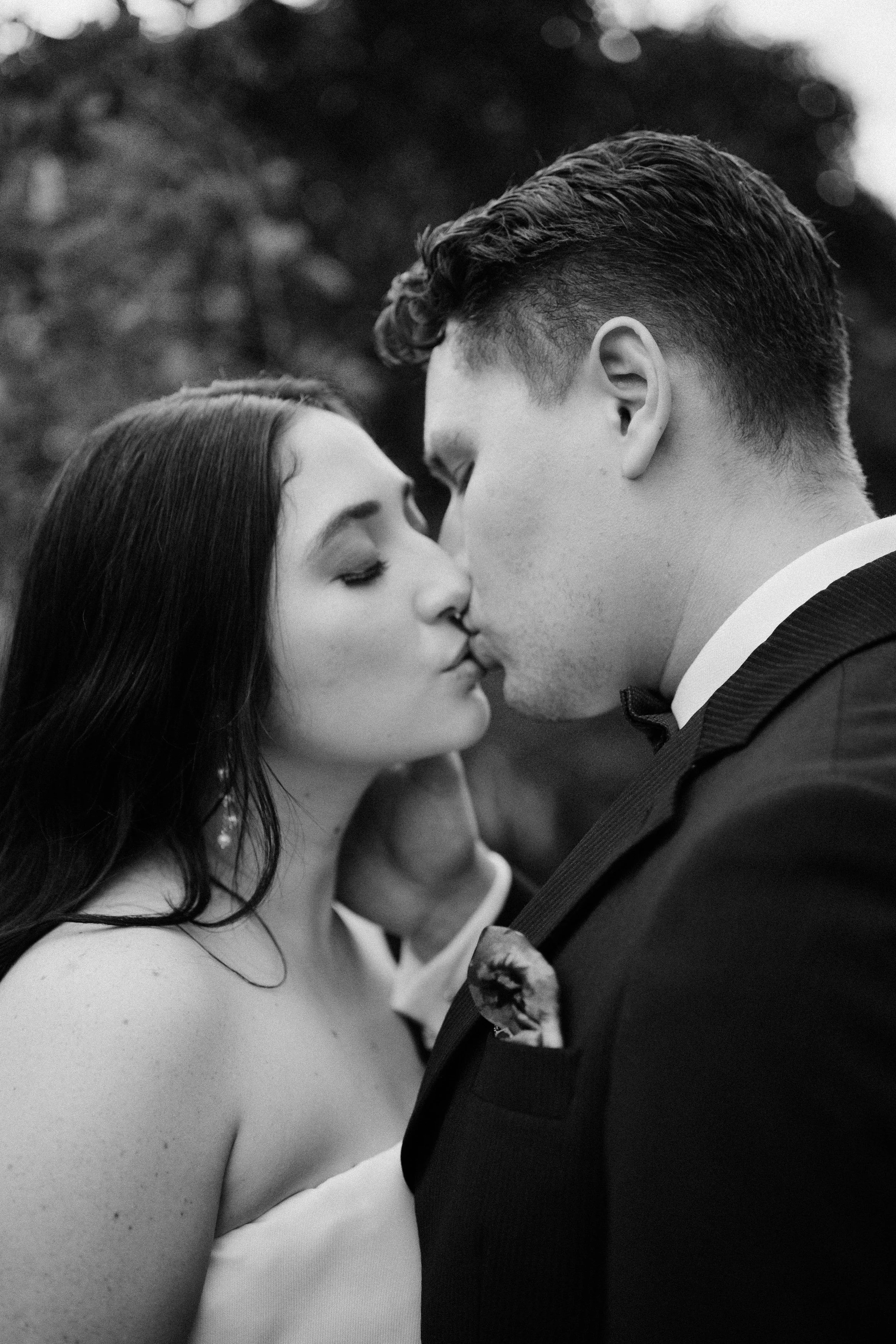 Pareja enamorada compartiendo un beso en blanco y negro, vista de perfil, en un ambiente natural.