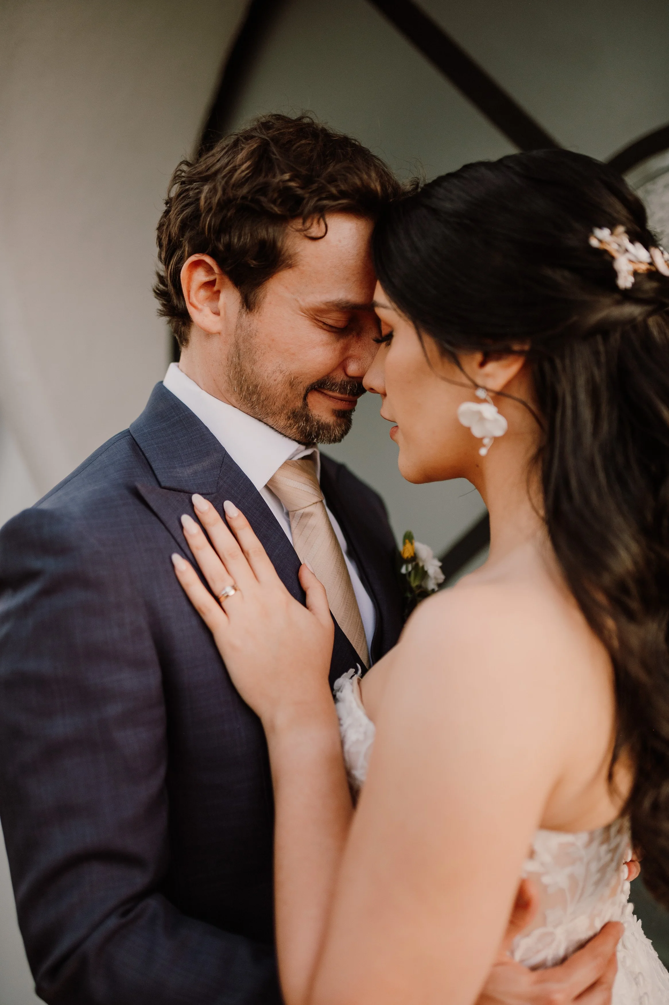 Pareja de novios en un beso con la frente tocándose, vestido de novia y traje de novio en una escena romántica.