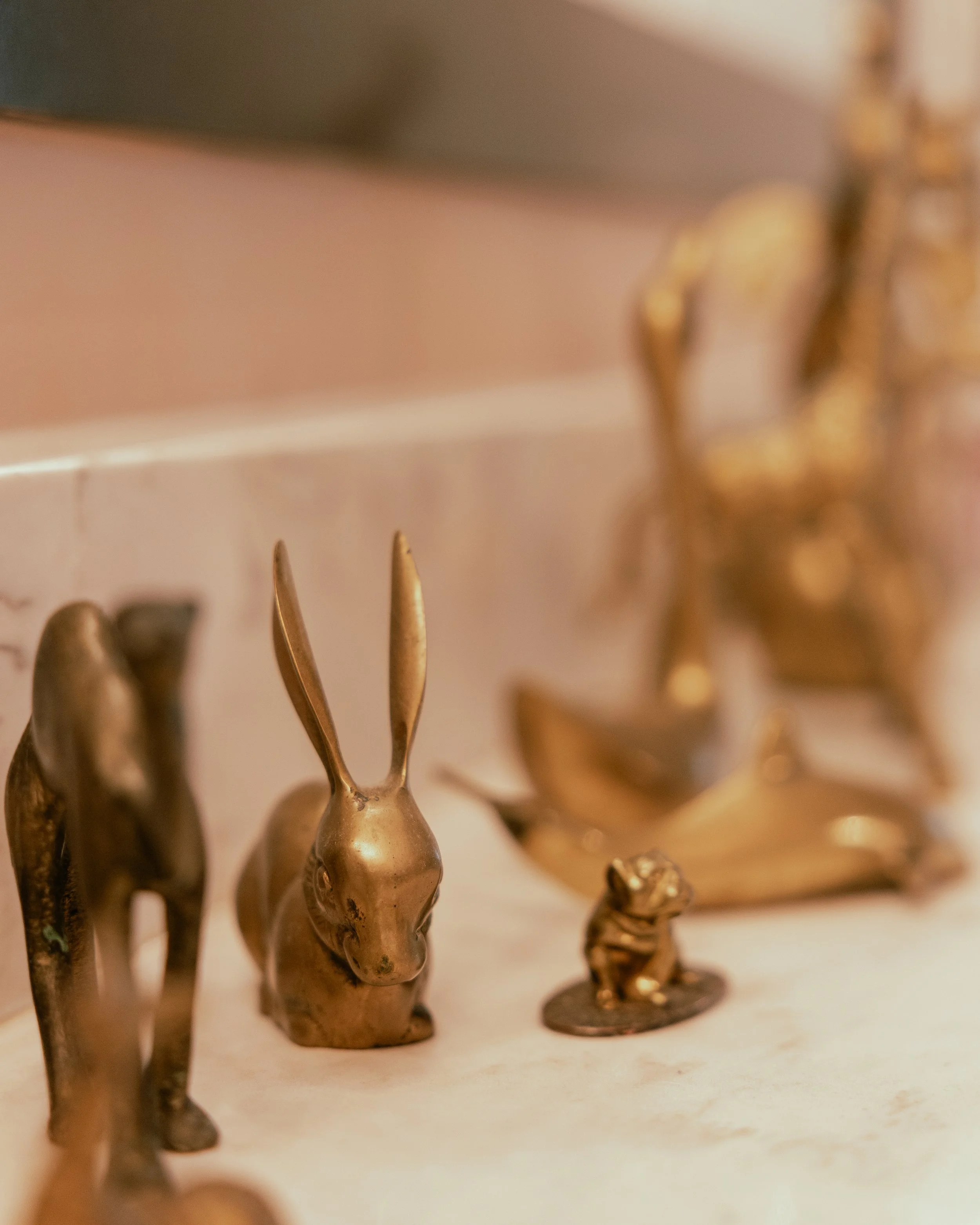 Collection of small brass animal figurines, including a rabbit, a bear, and other animals, displayed on a light-colored surface.