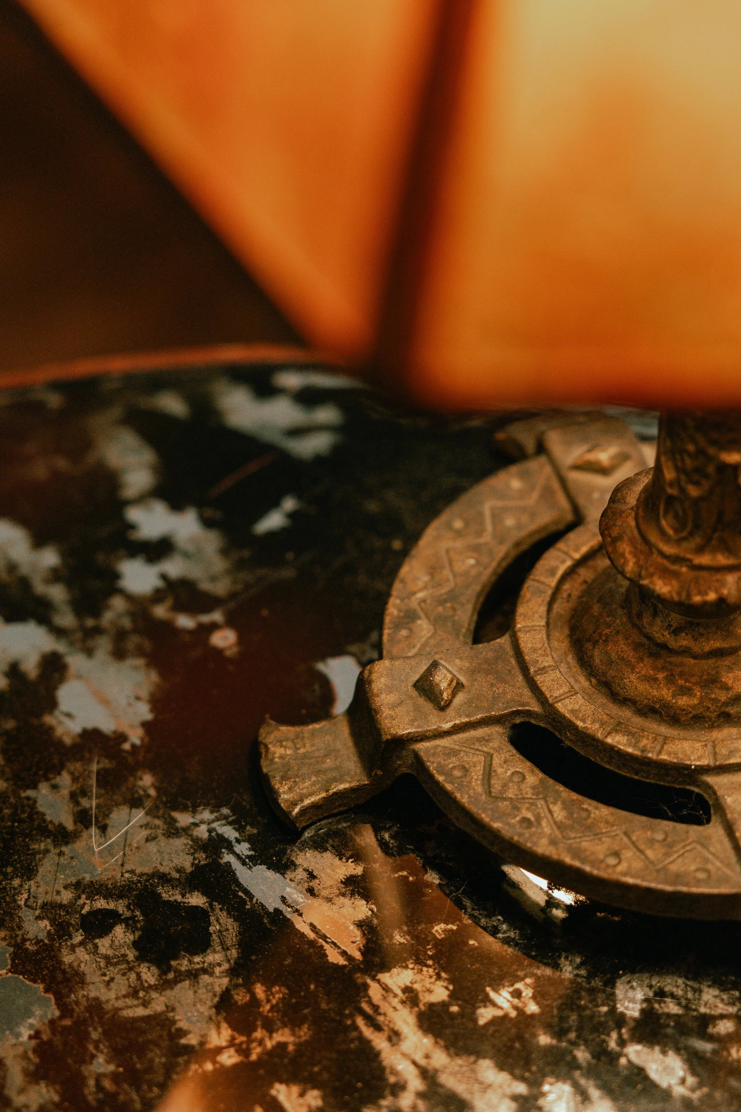 Close-up of a vintage, rusty compass resting on a worn, multicolored surface, with blurred orange background.