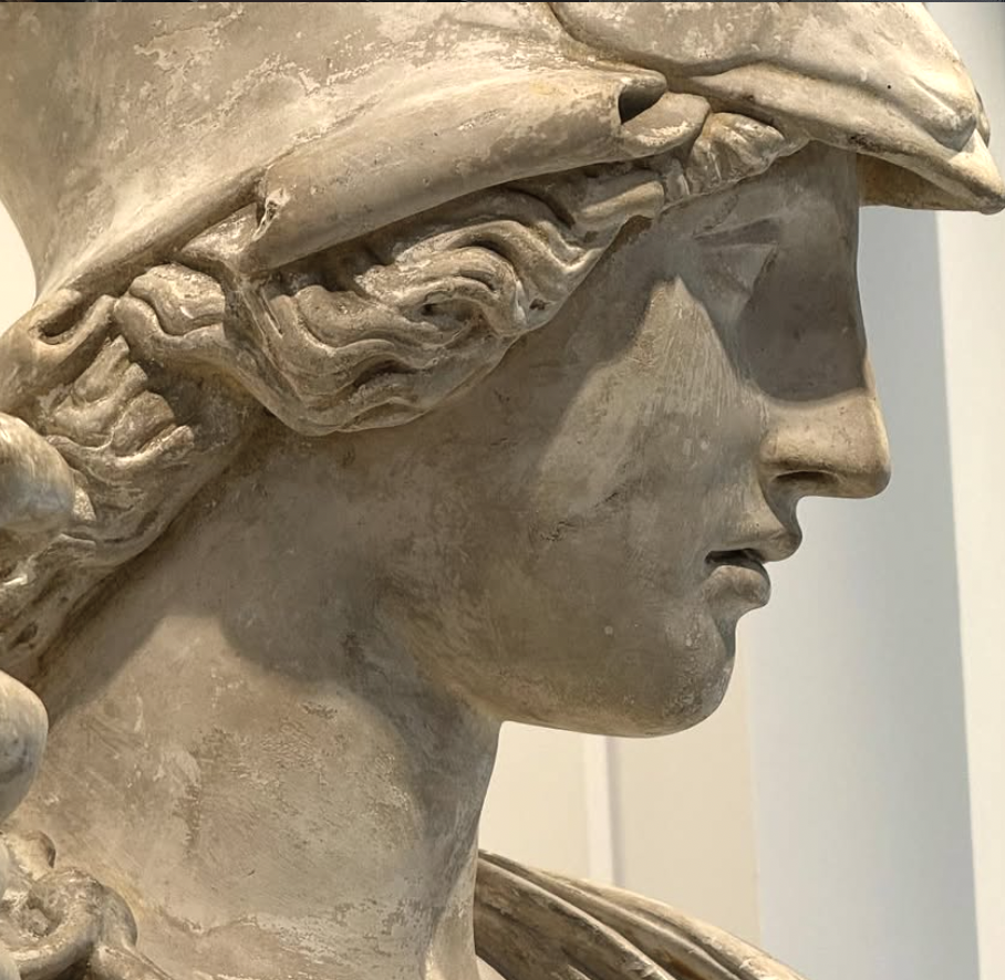 Close-up of a classical-style sculpture of a woman with curly hair and a prominent nose, likely made of marble or similar material.