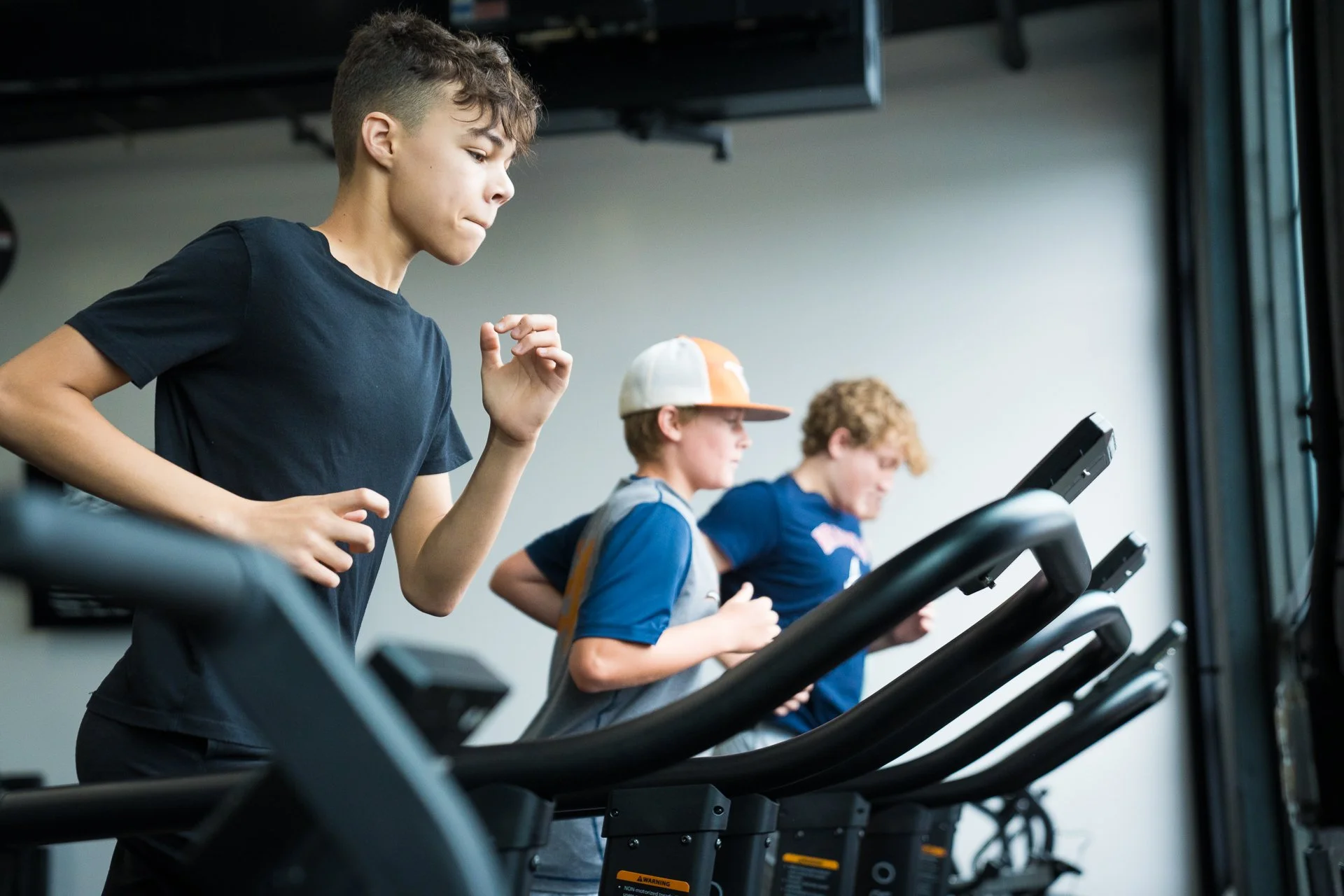 Three boys running on treadmills in a gym.