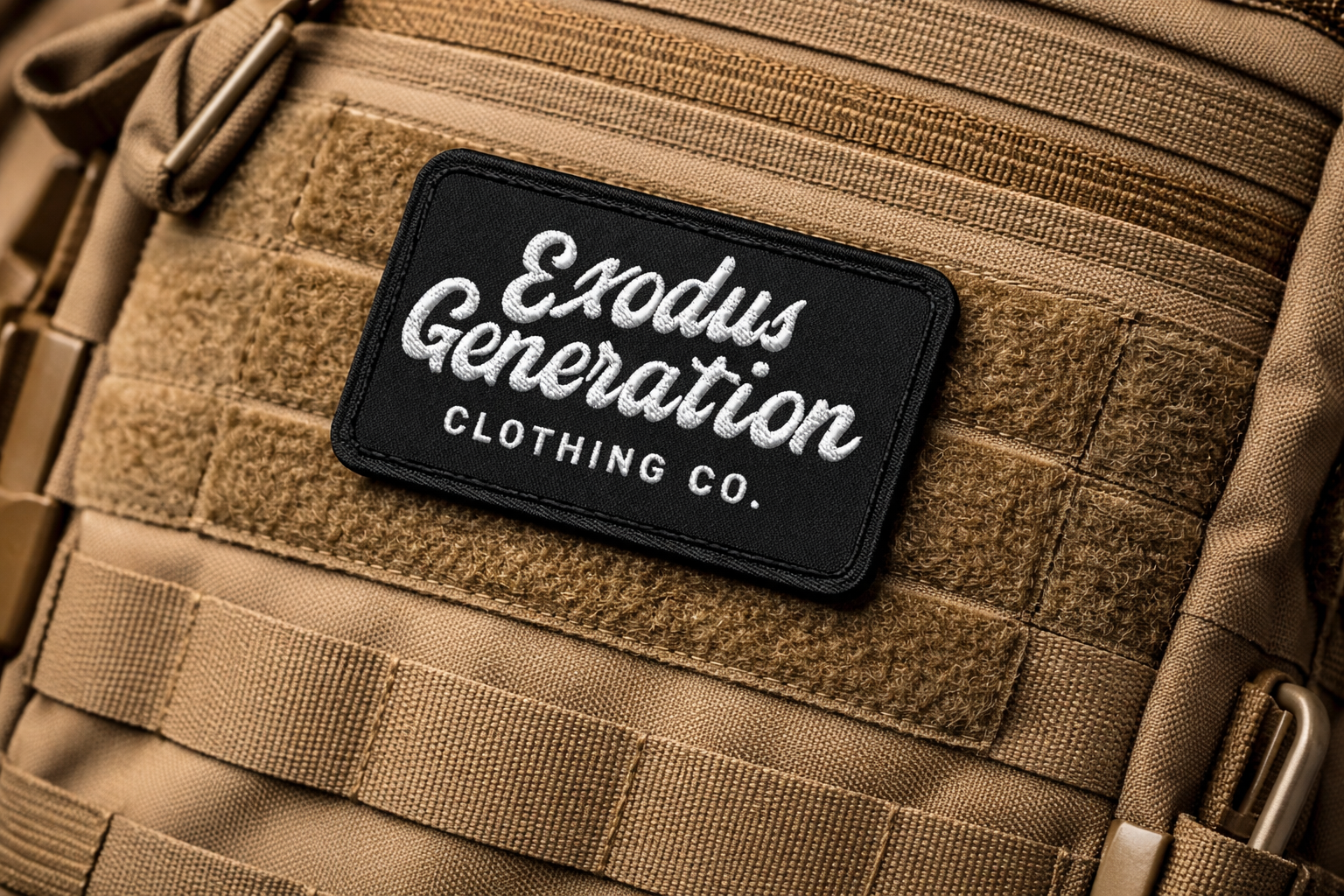 Close-up of a tan tactical backpack with a black patch reading 'Exodus Generation Clothing Co.' sewn onto it.