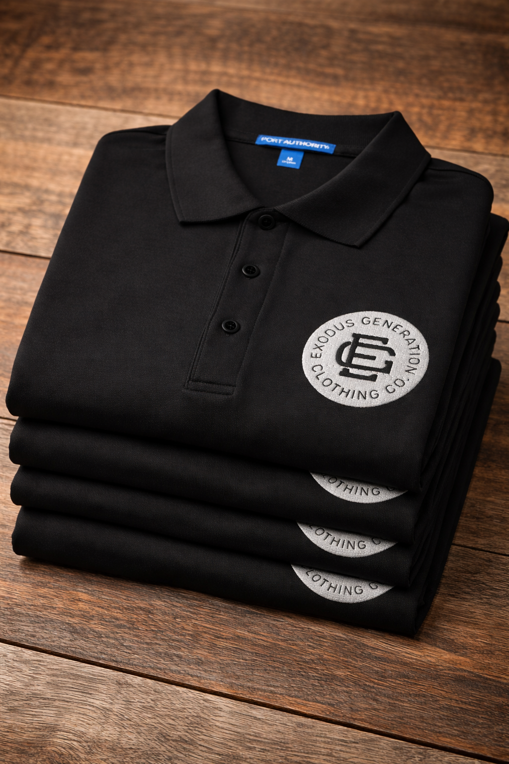 Stacked black polo shirts with a logo from Exodus Generation Clothing Co. placed on a wooden surface.