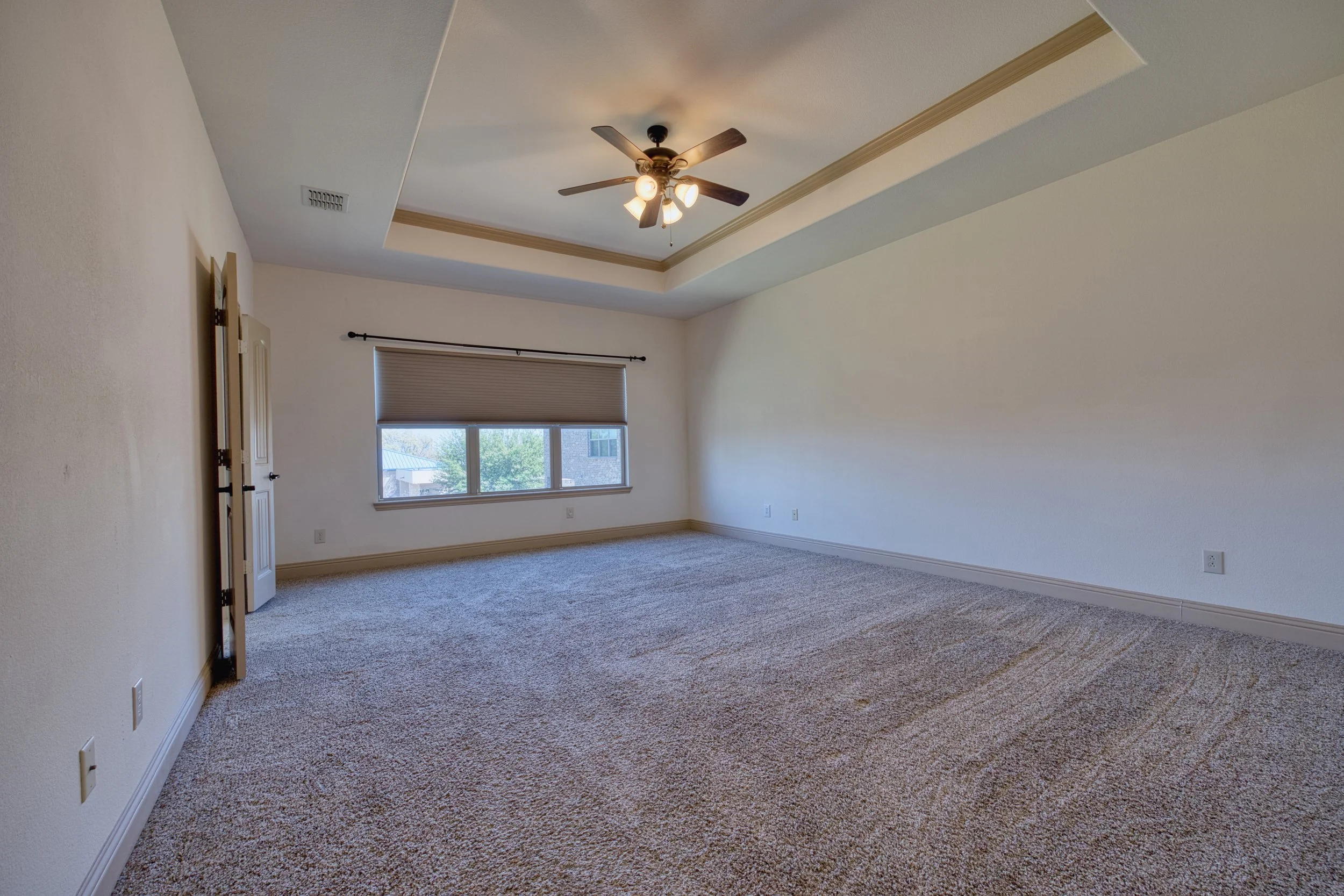 Empty room with beige carpet, white walls, a window with blinds, a ceiling fan with light, and crown molding.