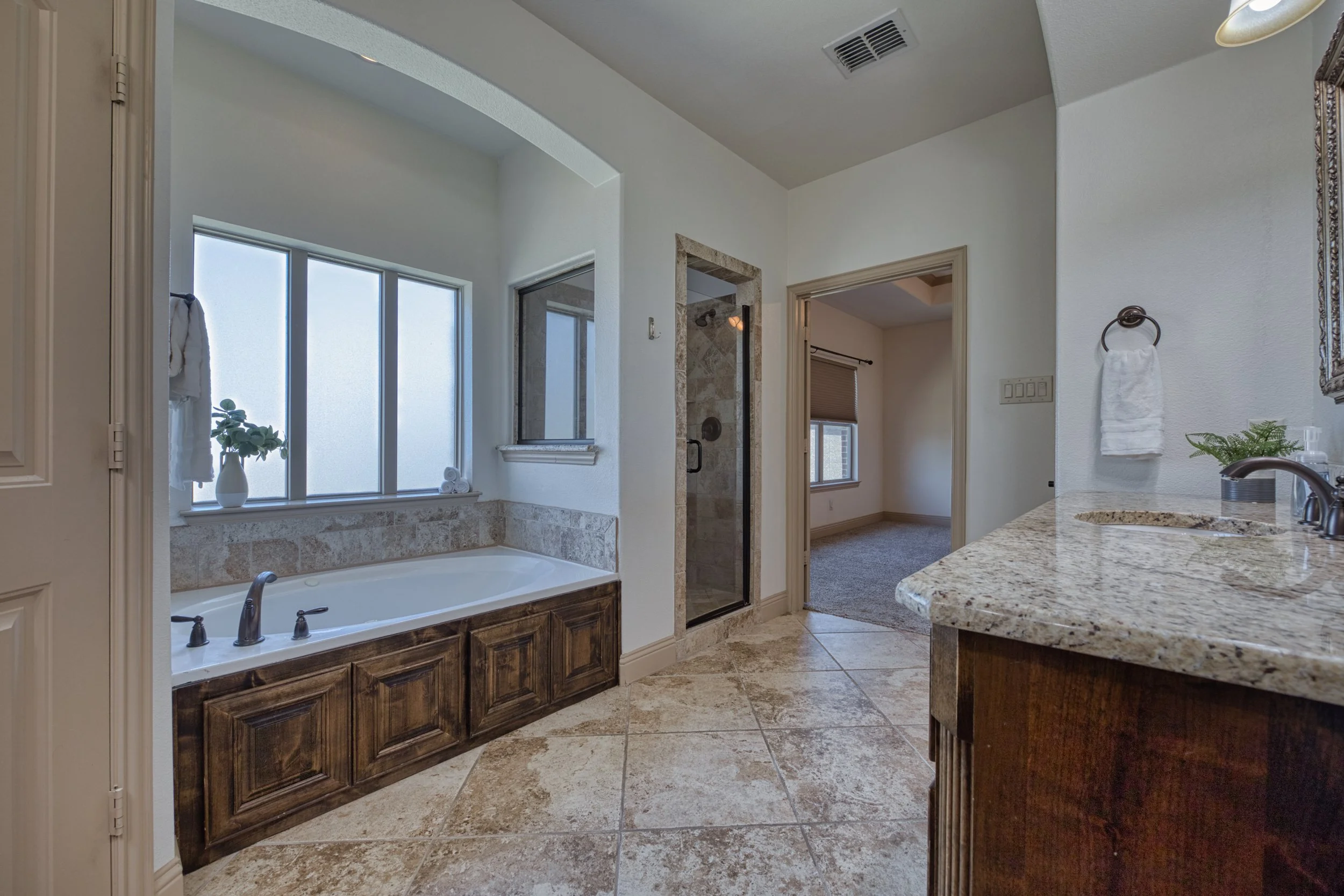 Bathroom with bathtub, glass-enclosed shower, granite countertop sink, frosted windows, and beige tiled flooring.